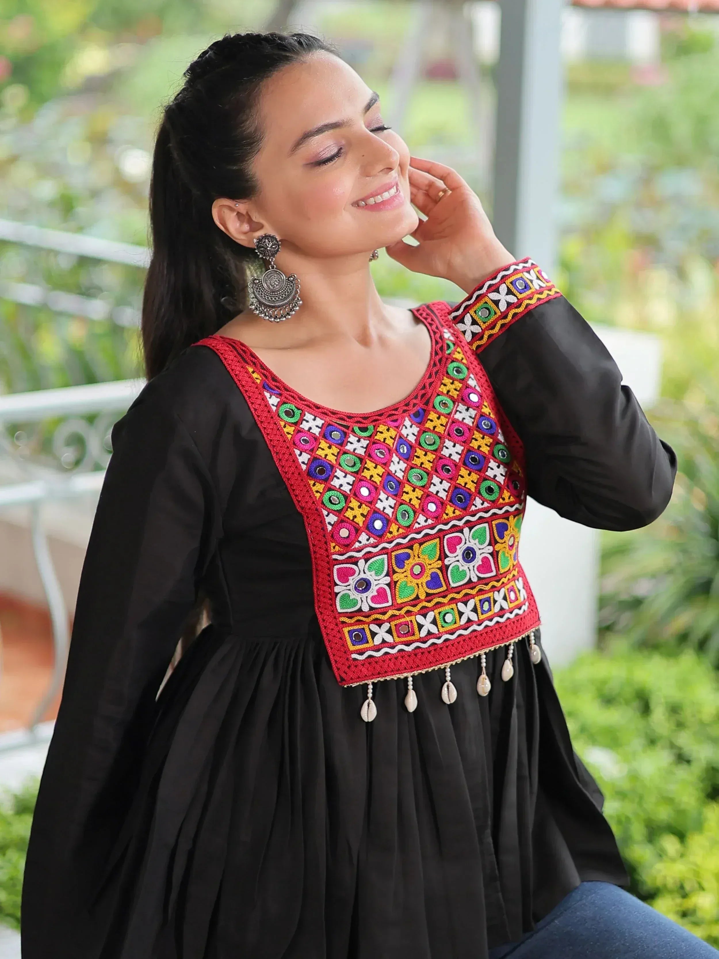 Black ethnic kurti with colorful mirror embroidery and shell tassels, paired with statement earrings