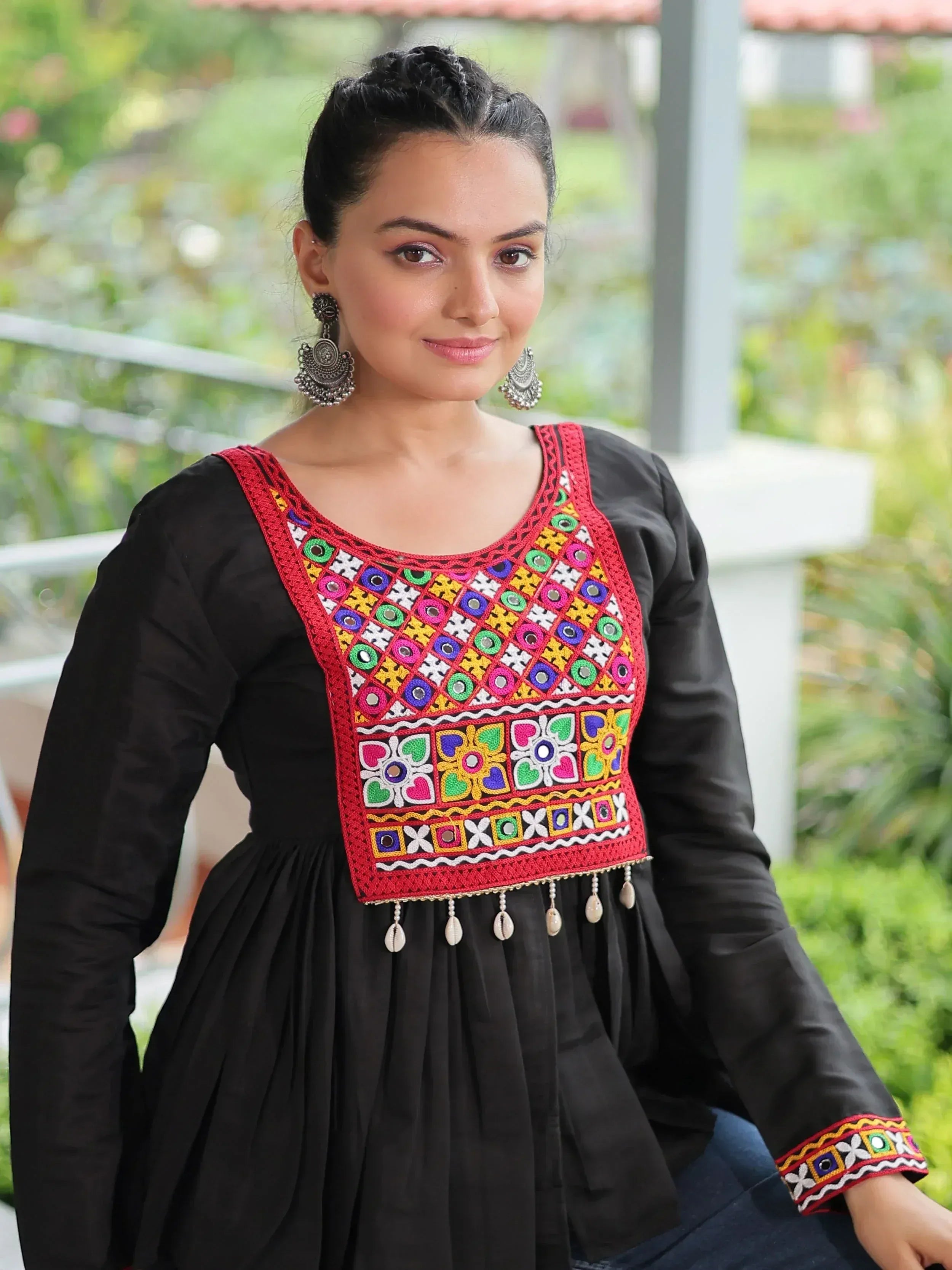 Black ethnic kurti with colorful mirror work and shell tassels, paired with statement earrings
