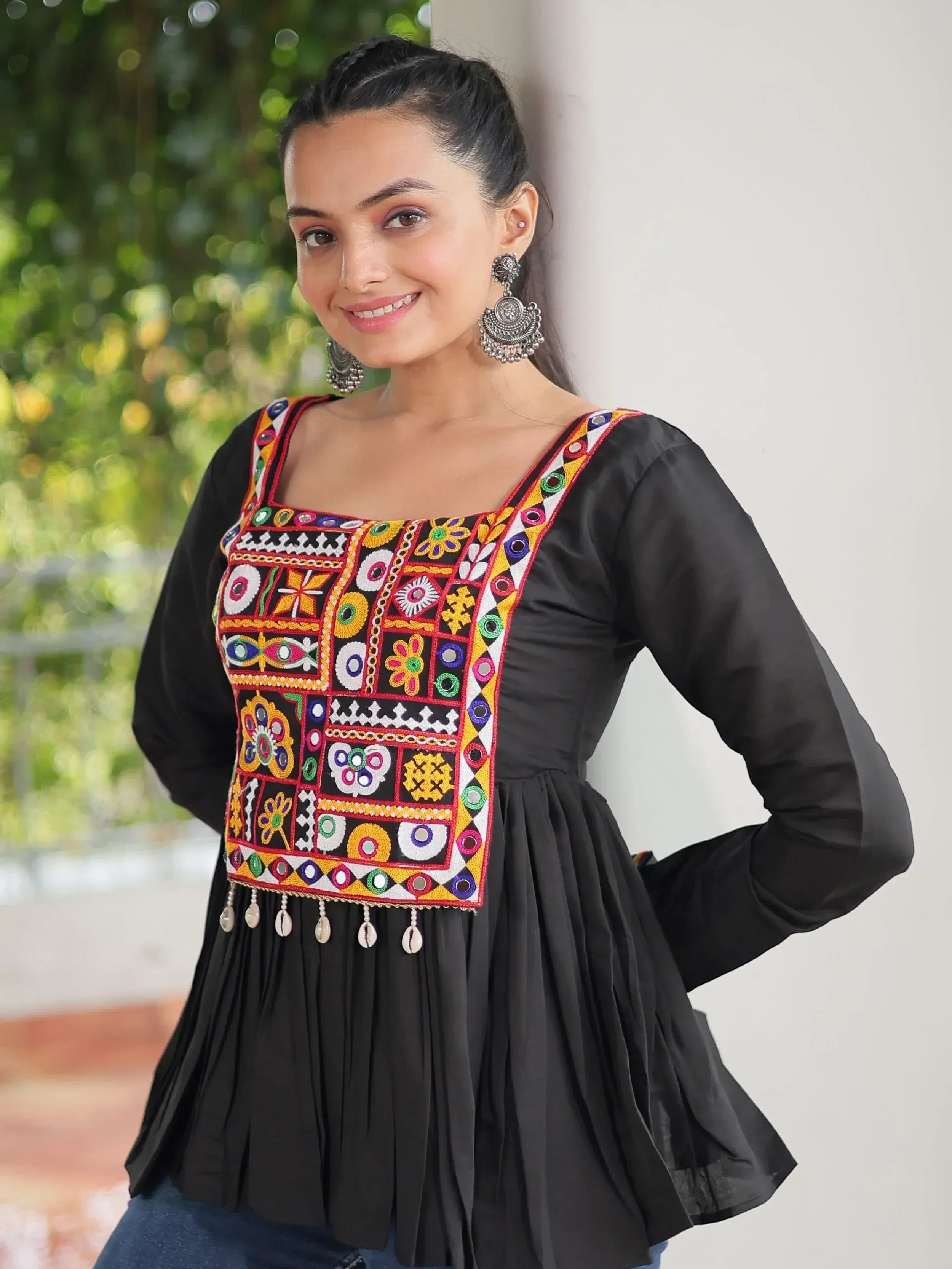 Black ethnic top with colorful mirror embroidery and shell tassels, paired with statement earrings.