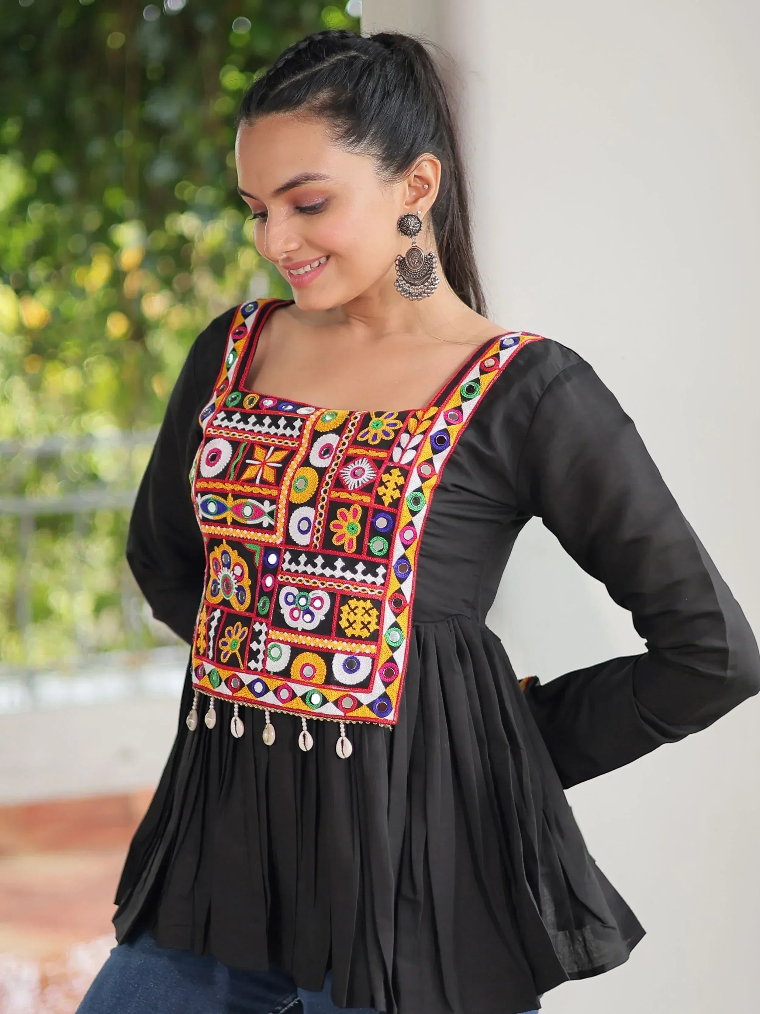 Black ethnic kurti with colorful mirror embroidery and shell tassels, paired with statement earrings.