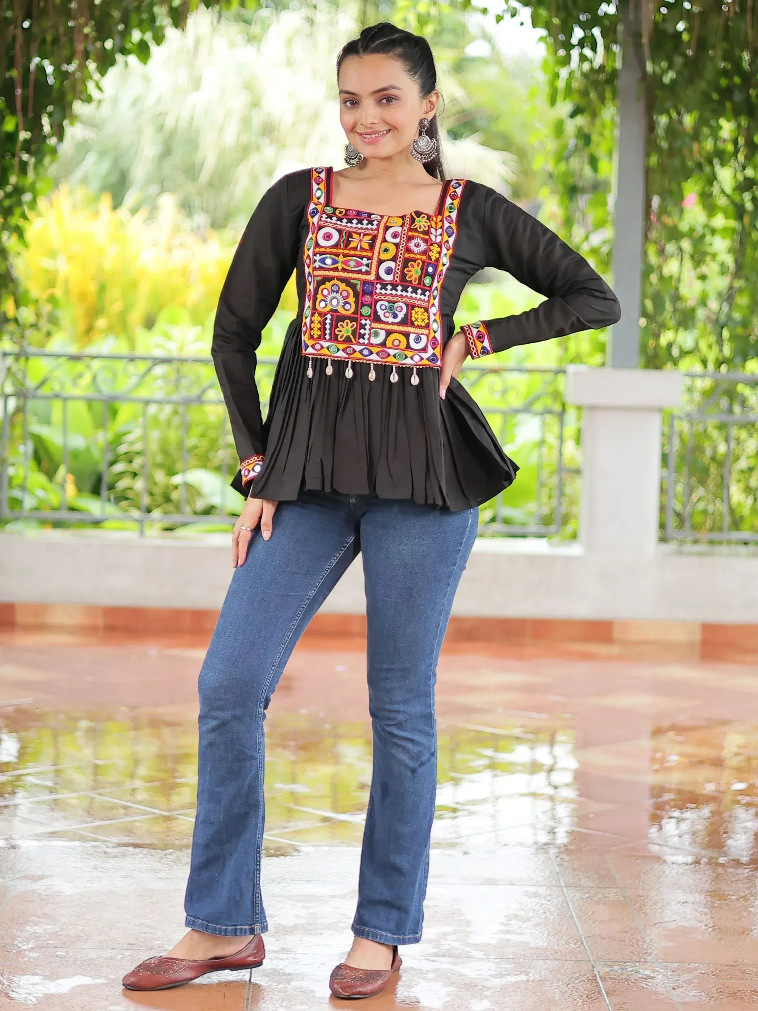 Black embroidered ethnic top with colorful mirror work, paired with blue jeans and brown flats, perfect for casual wear.