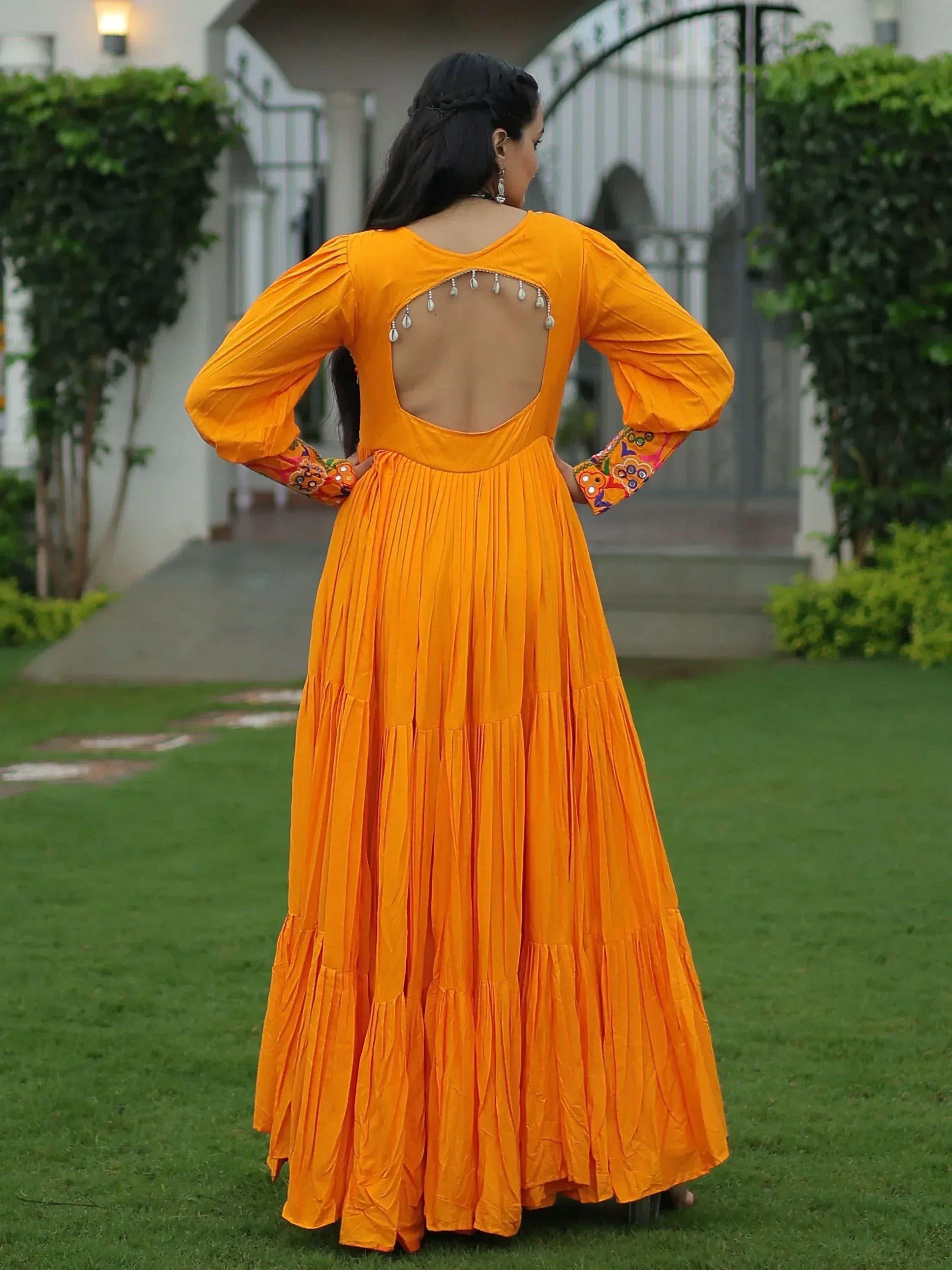Vibrant orange ethnic gown with back cutout, embellished sleeves, and pleated skirt, perfect for Indian occasions.
