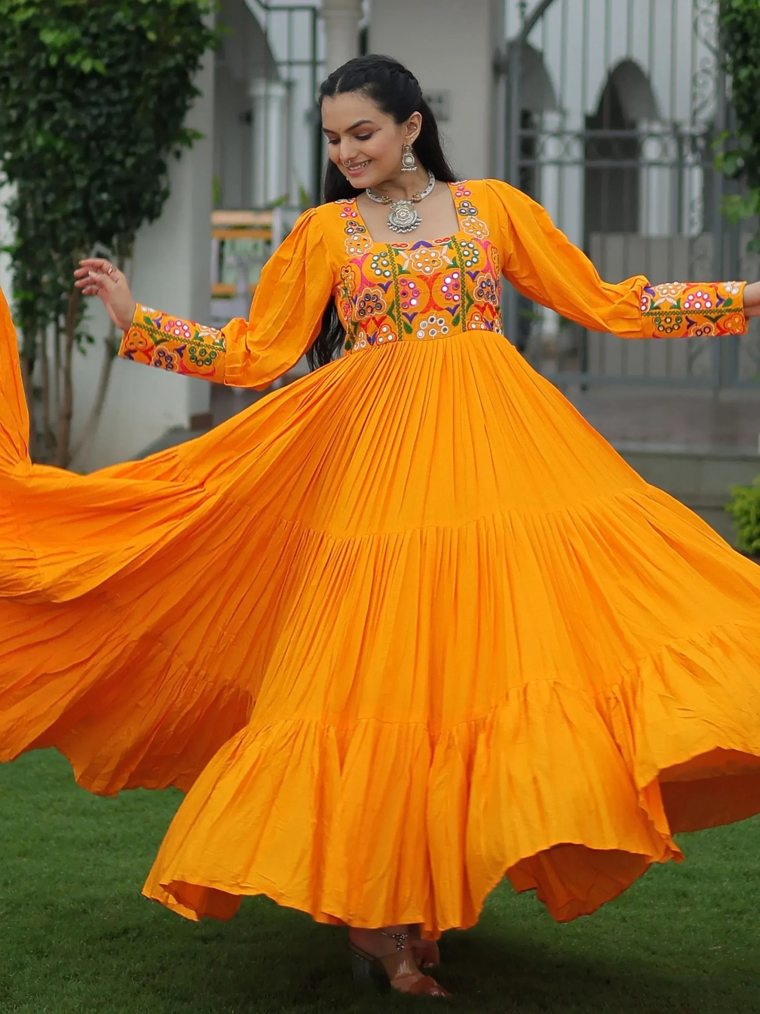Vibrant orange ethnic gown with floral embroidery, pleated skirt, and puff sleeves for festive occasions