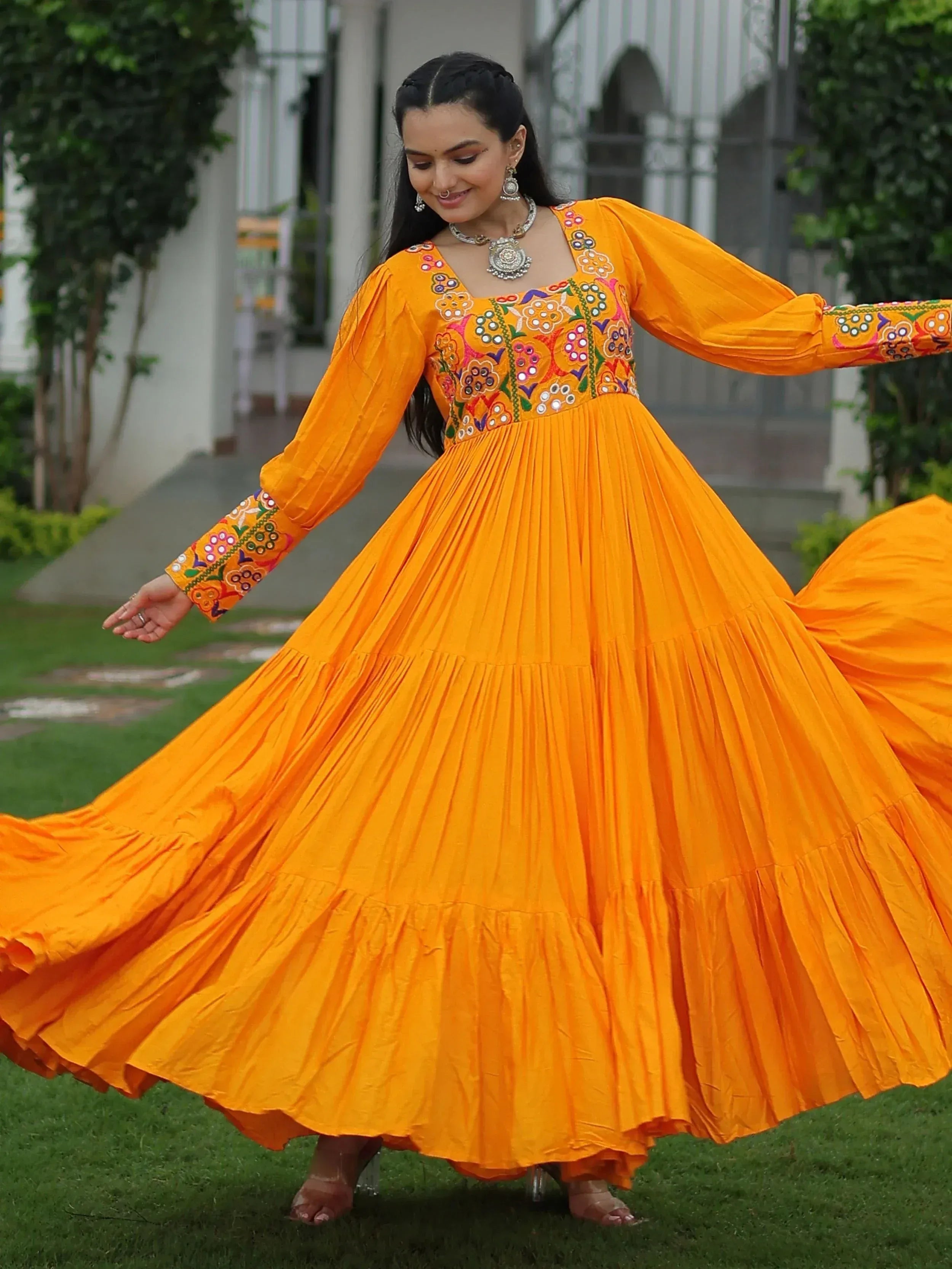 Woman twirling in vibrant orange ethnic gown with floral embroidery, perfect for festive occasions.