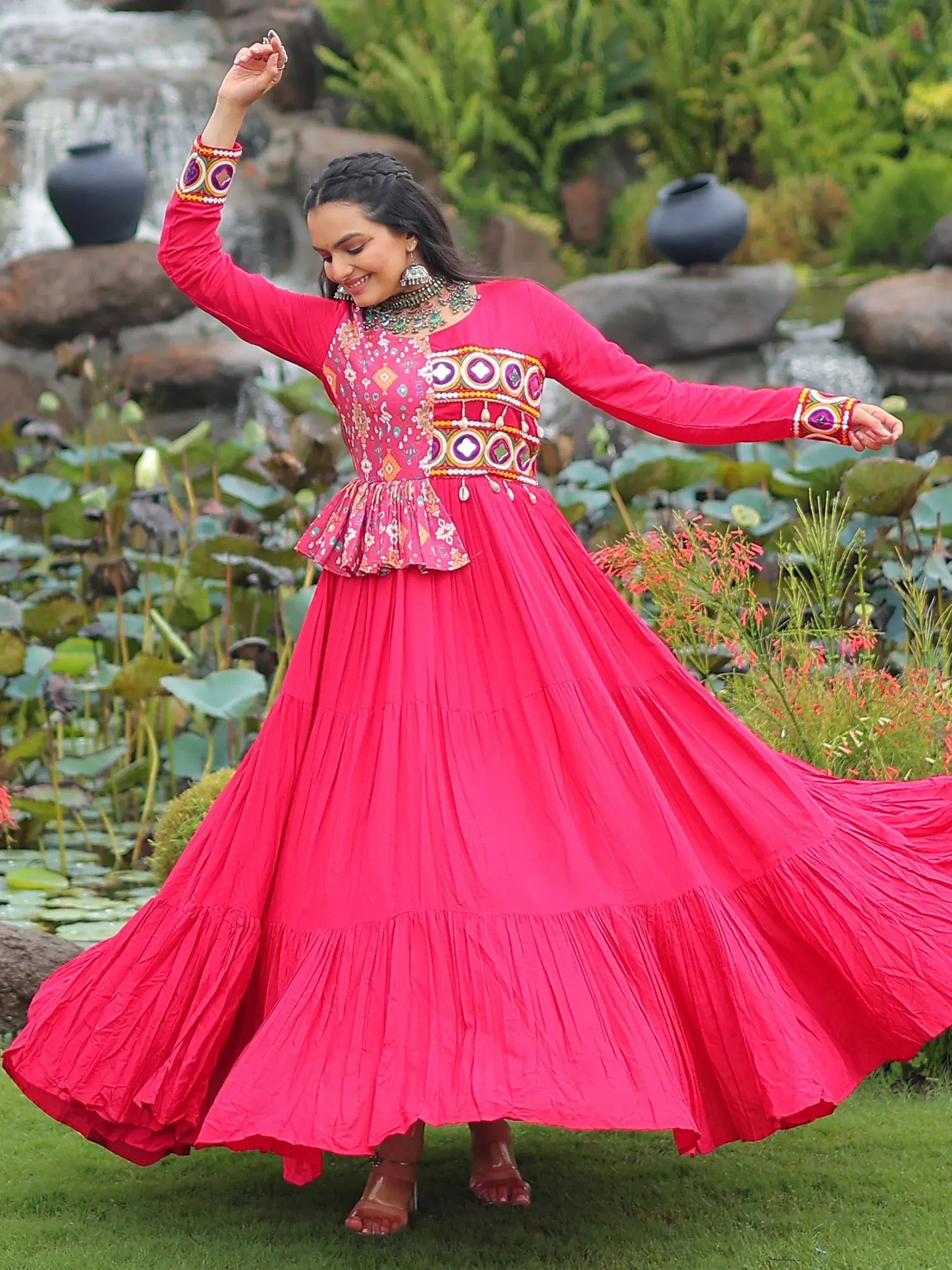 Woman twirling in vibrant pink embroidered ethnic gown with pleated skirt, garden backdrop
