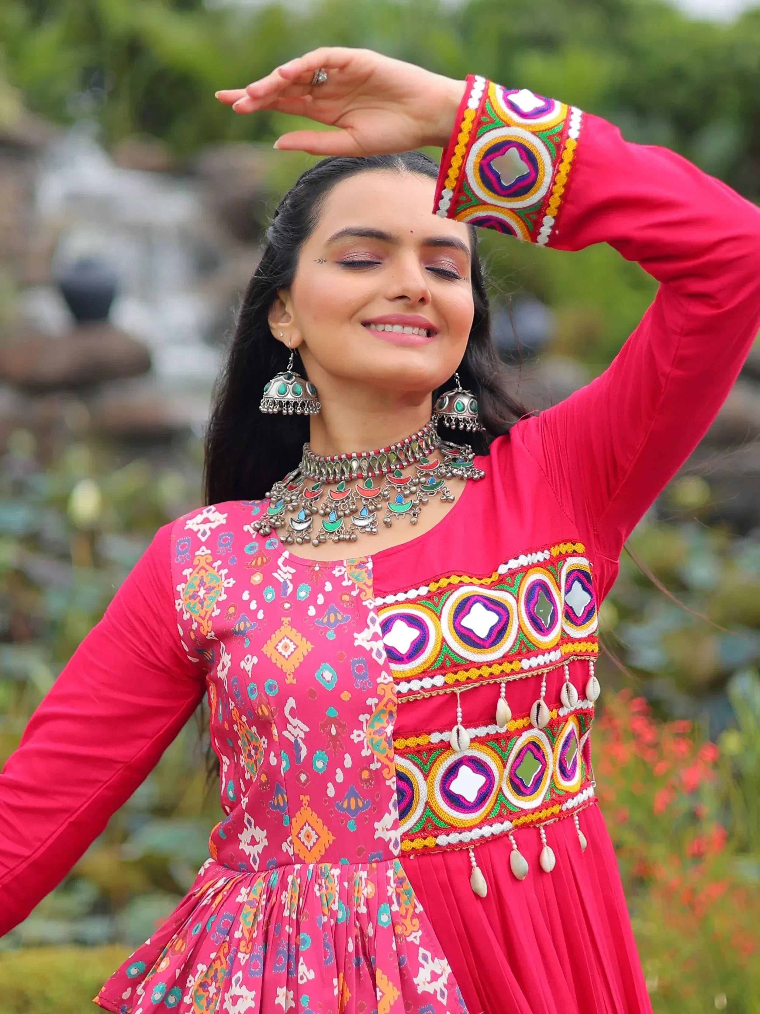 Woman in vibrant pink ethnic gown with mirror work and traditional jewelry, perfect for Indian festive occasions