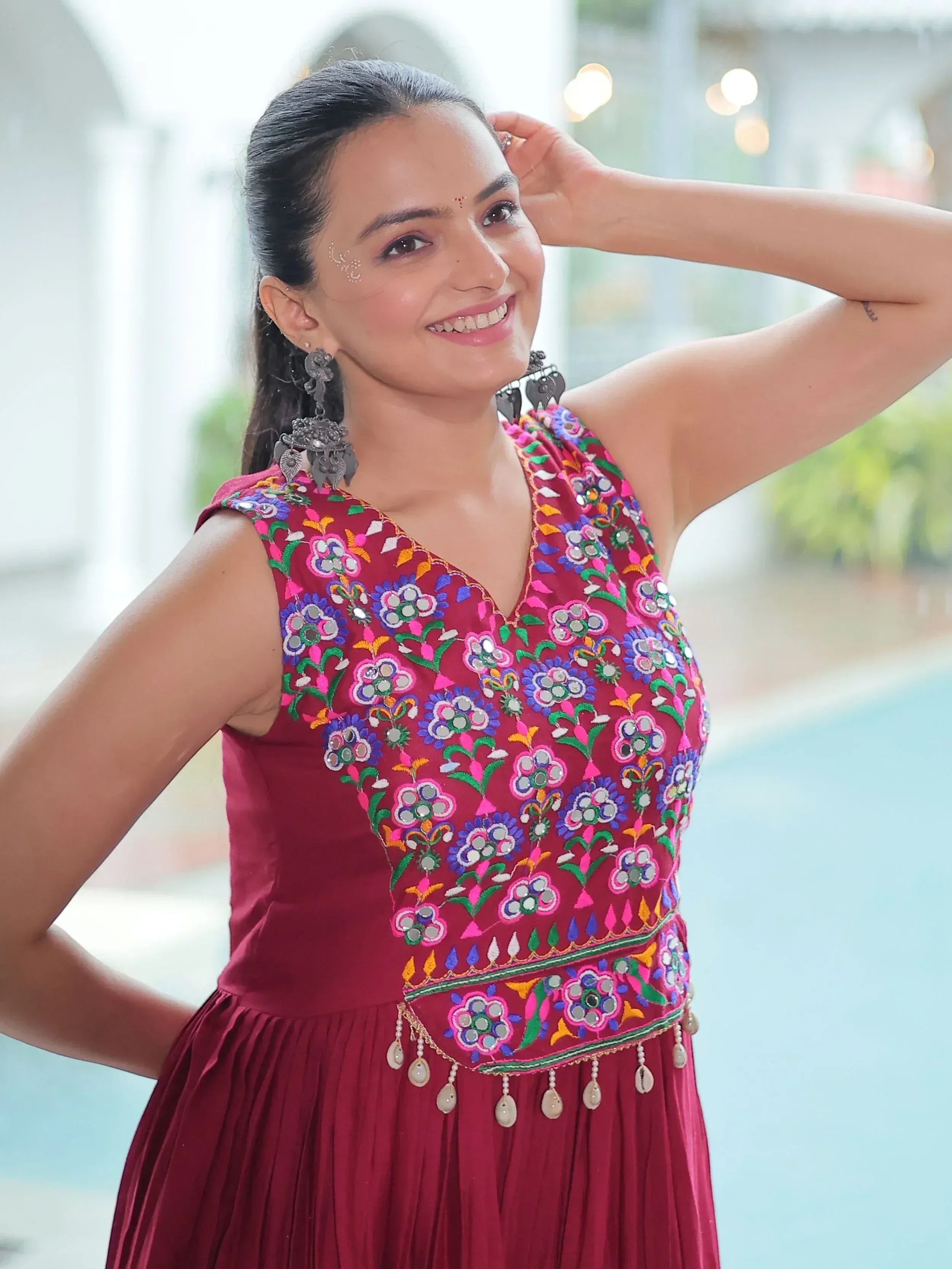 Woman in maroon ethnic gown with colorful floral embroidery and mirror work, perfect for Indian occasions