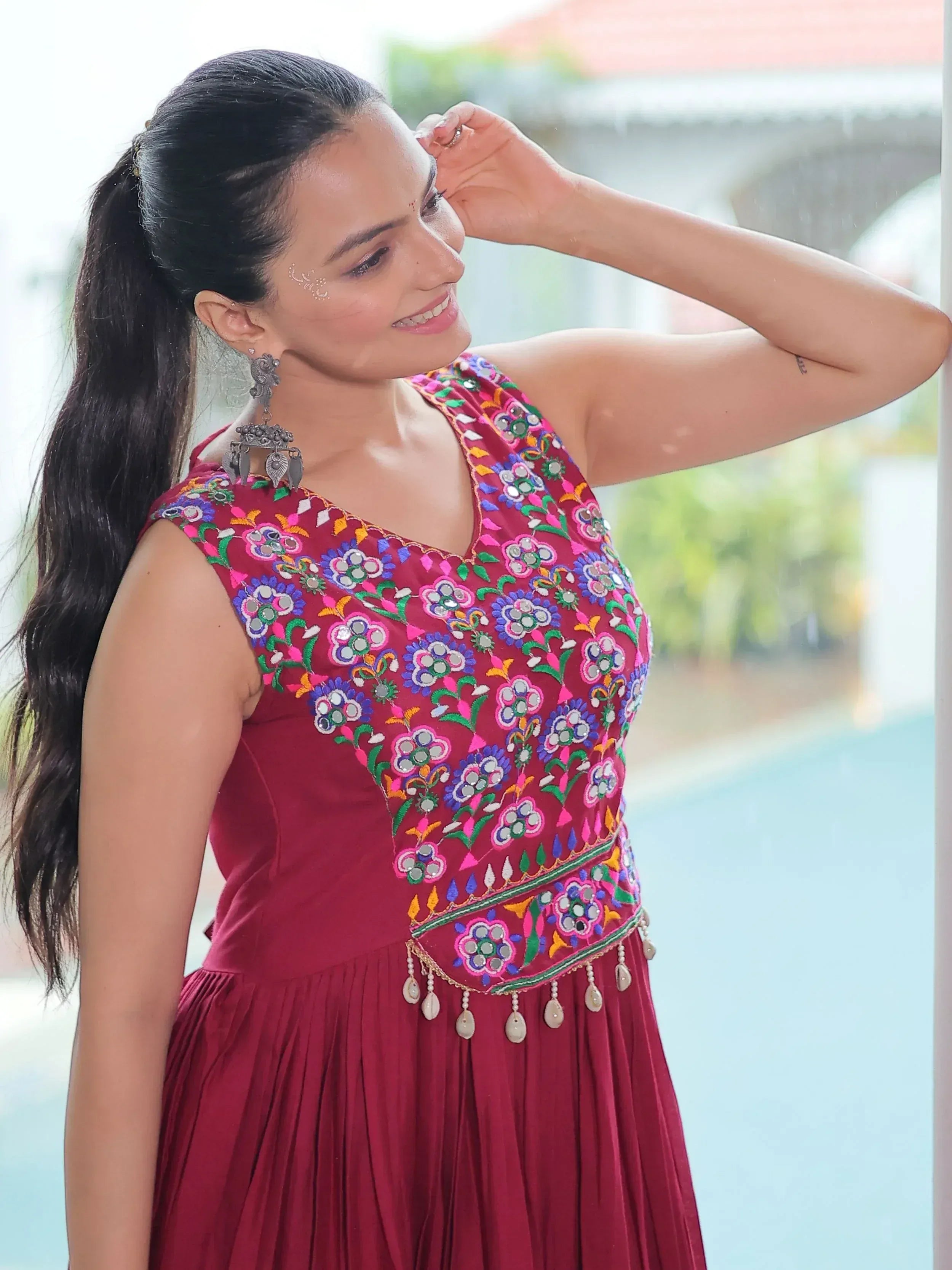 Woman in maroon ethnic gown with colorful floral embroidery and mirror work, perfect for Indian occasions