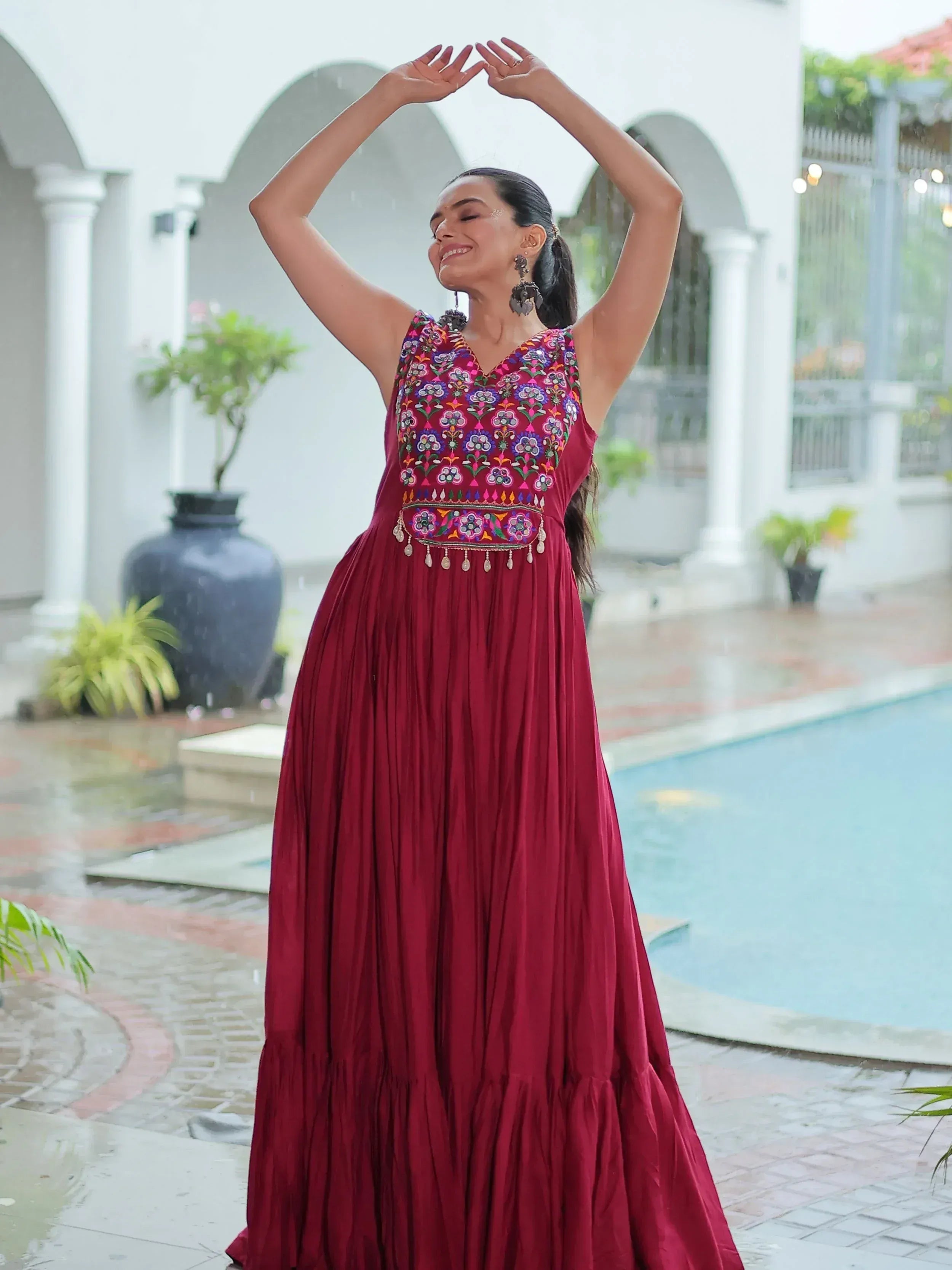 Woman in maroon embroidered ethnic gown with floral motifs, standing by poolside in rain
