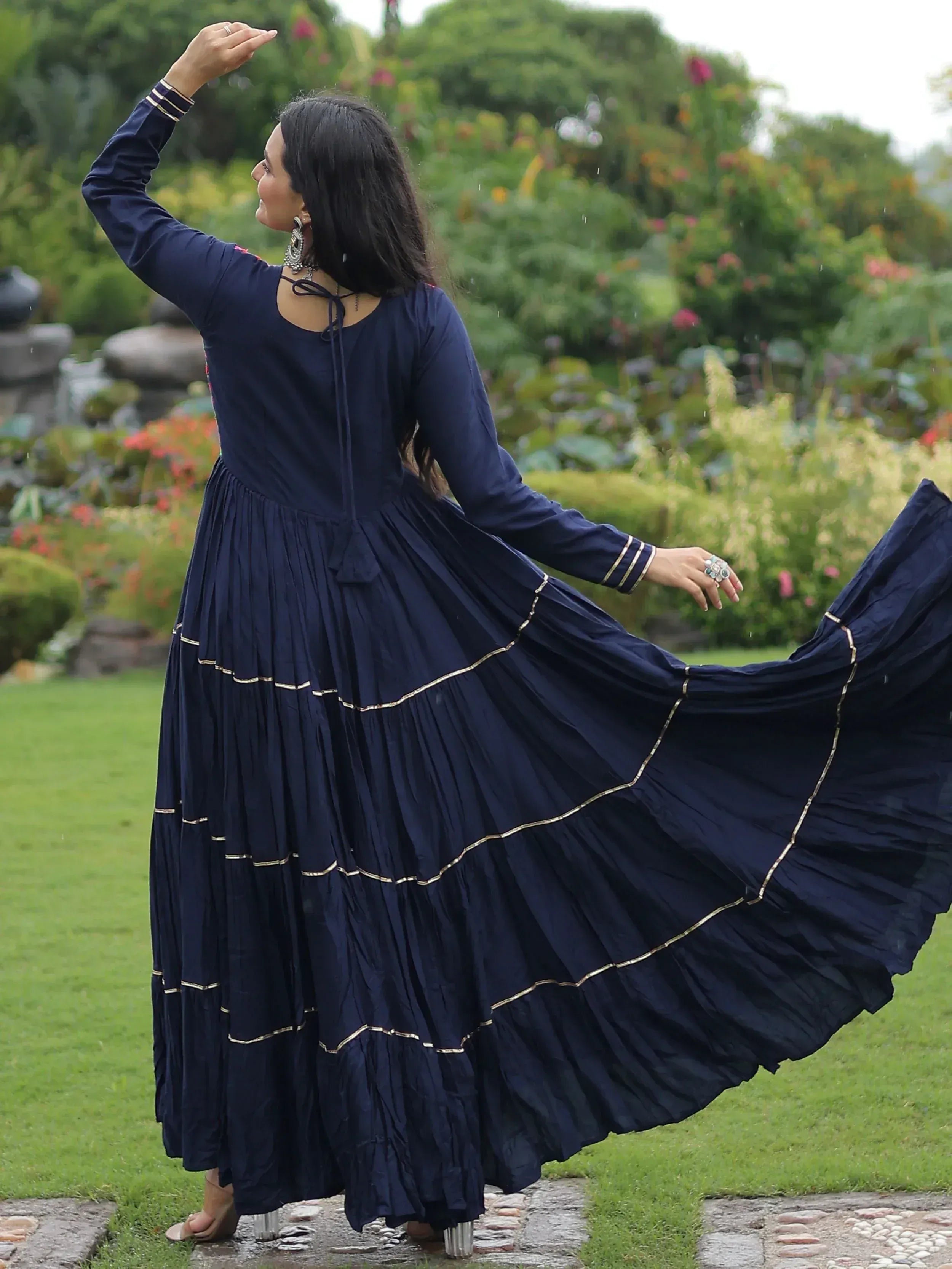 Navy blue ethnic gown with gold trim, flowing pleats, worn in garden setting