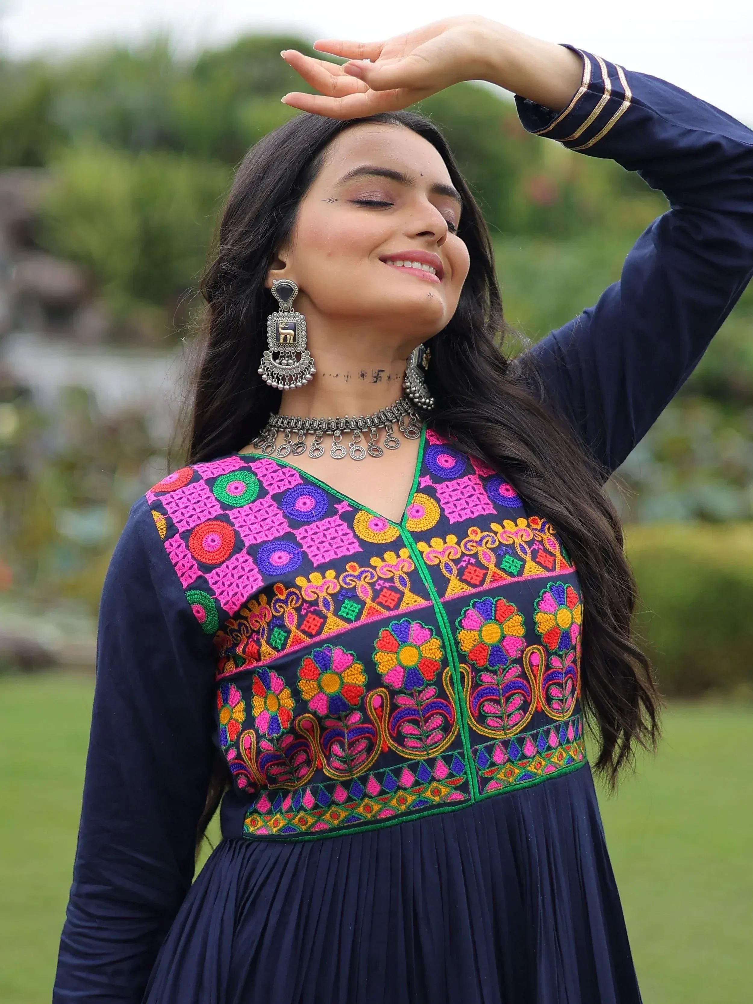 Woman in navy blue ethnic gown with vibrant floral embroidery, traditional jewelry, outdoors