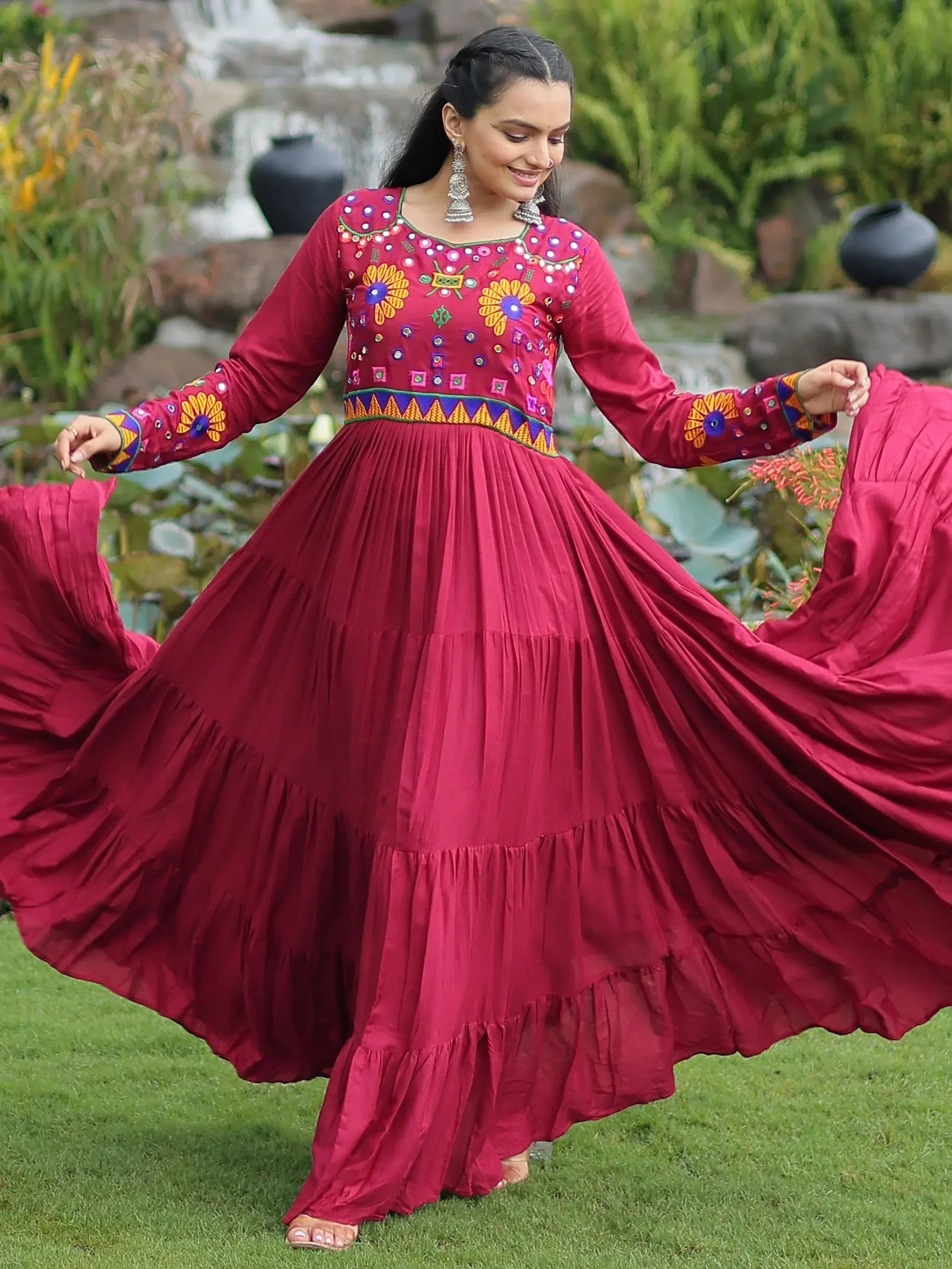Woman twirling in maroon ethnic gown with floral mirror work, perfect for Indian festivals and occasions.