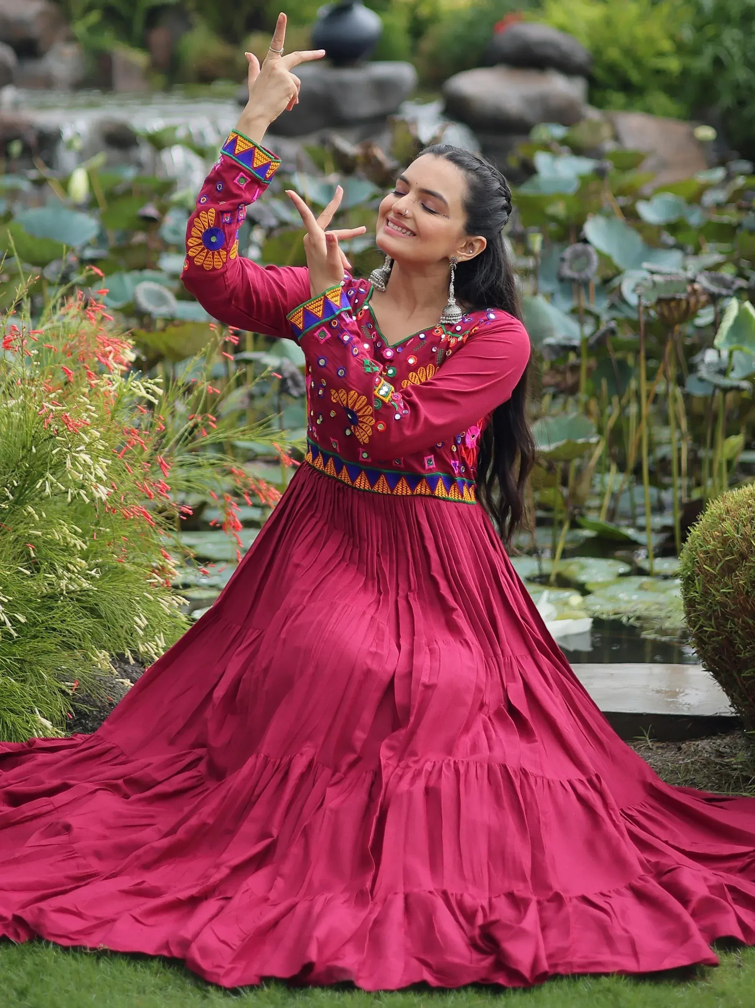 Woman in maroon ethnic gown with mirror work dancing near lotus pond
