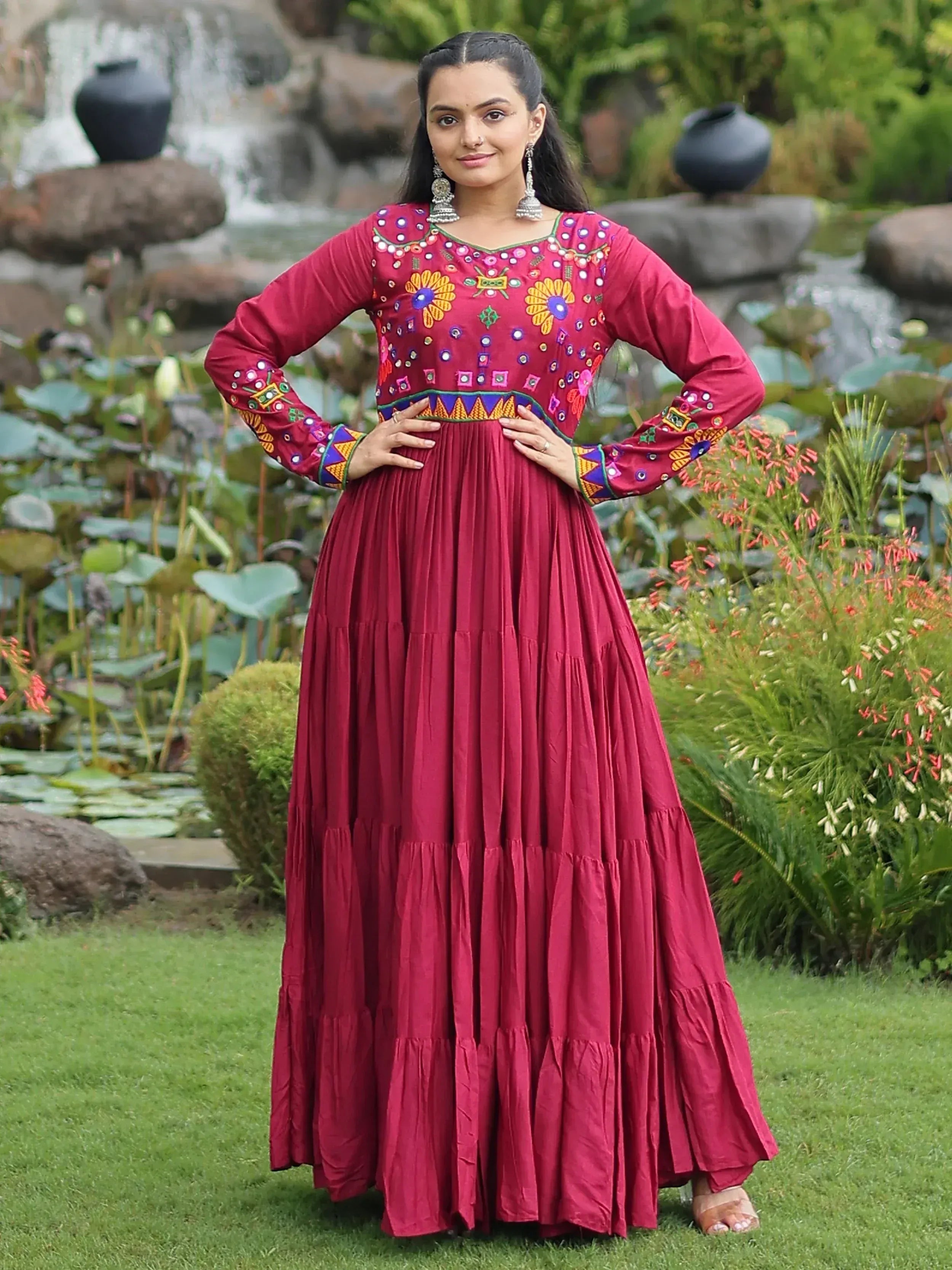 Woman in maroon ethnic gown with floral embroidery, standing in garden