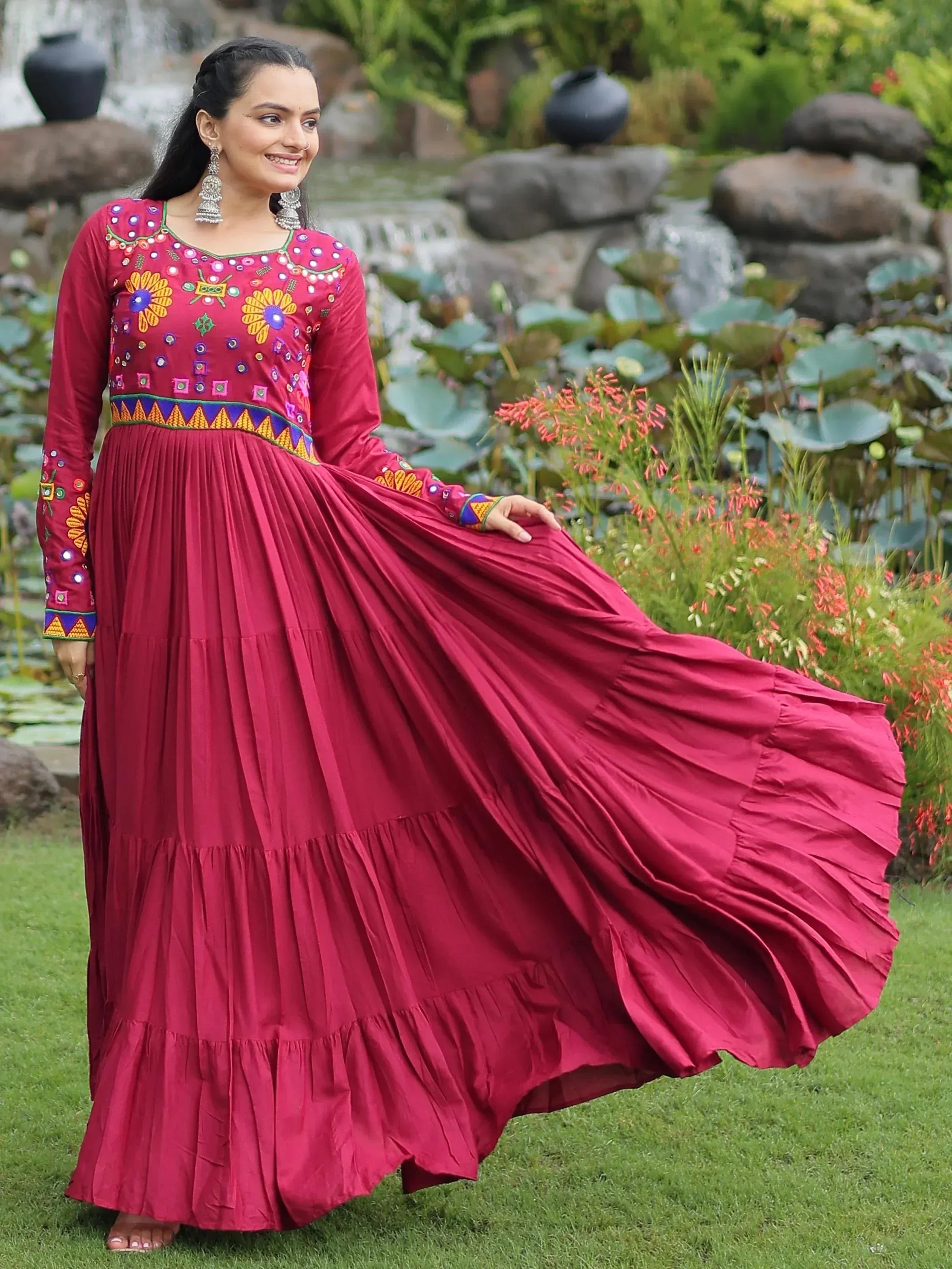 Woman in maroon ethnic gown with floral embroidery, standing in garden