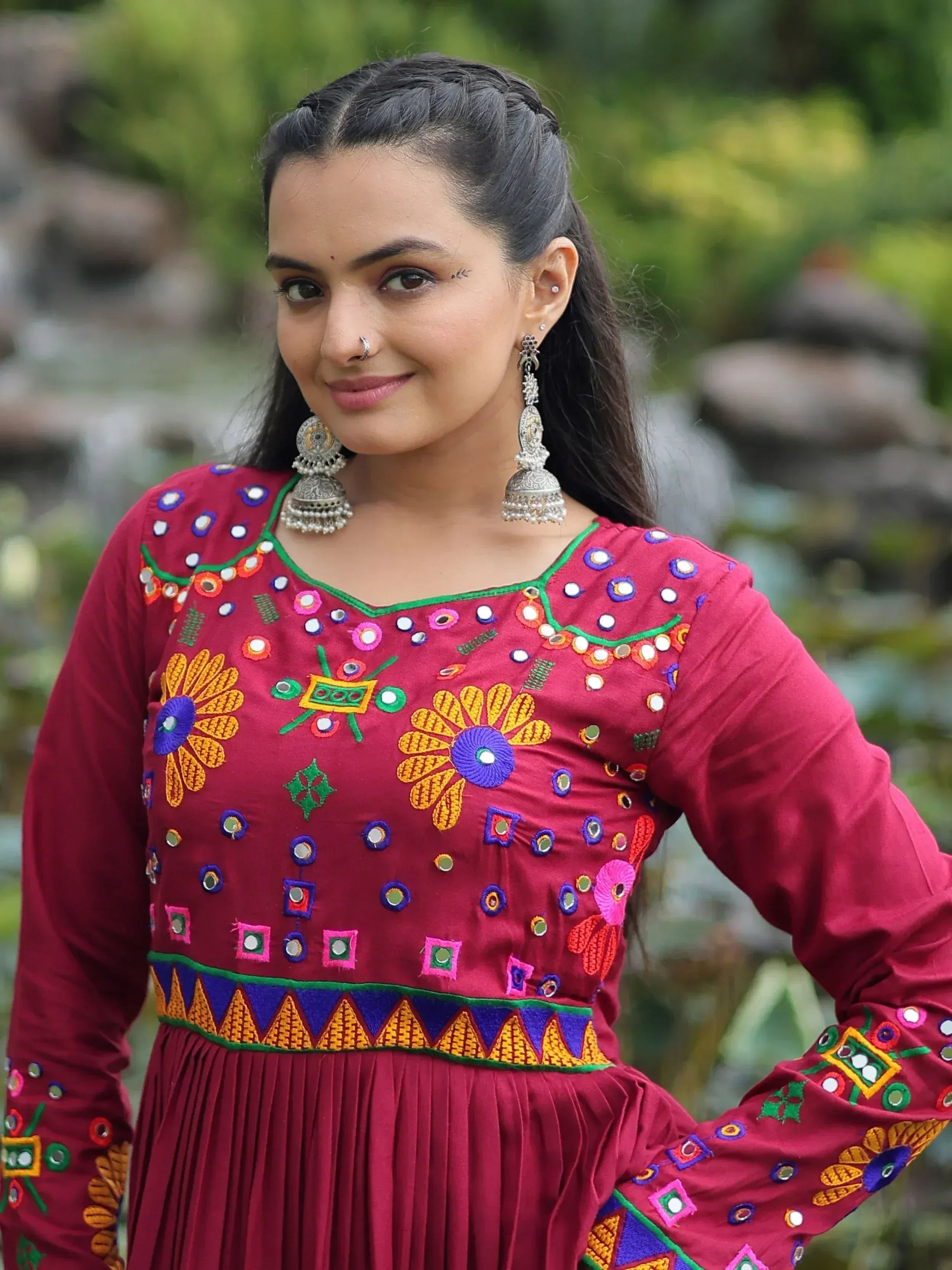 Woman in maroon ethnic gown with mirror work and floral embroidery, styled with jhumka earrings