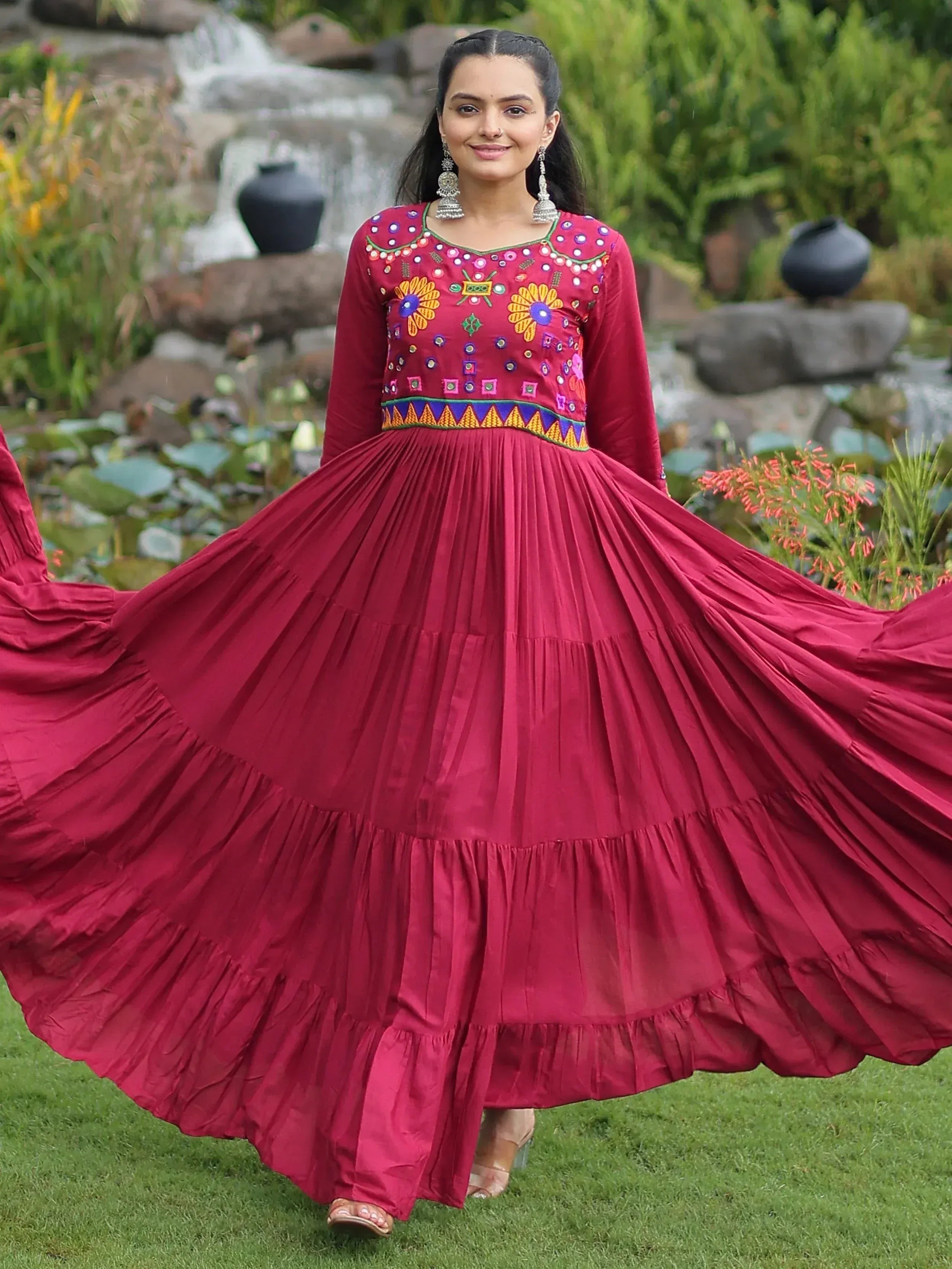 Woman in maroon ethnic gown with mirror work, twirling in garden, perfect for Indian occasions