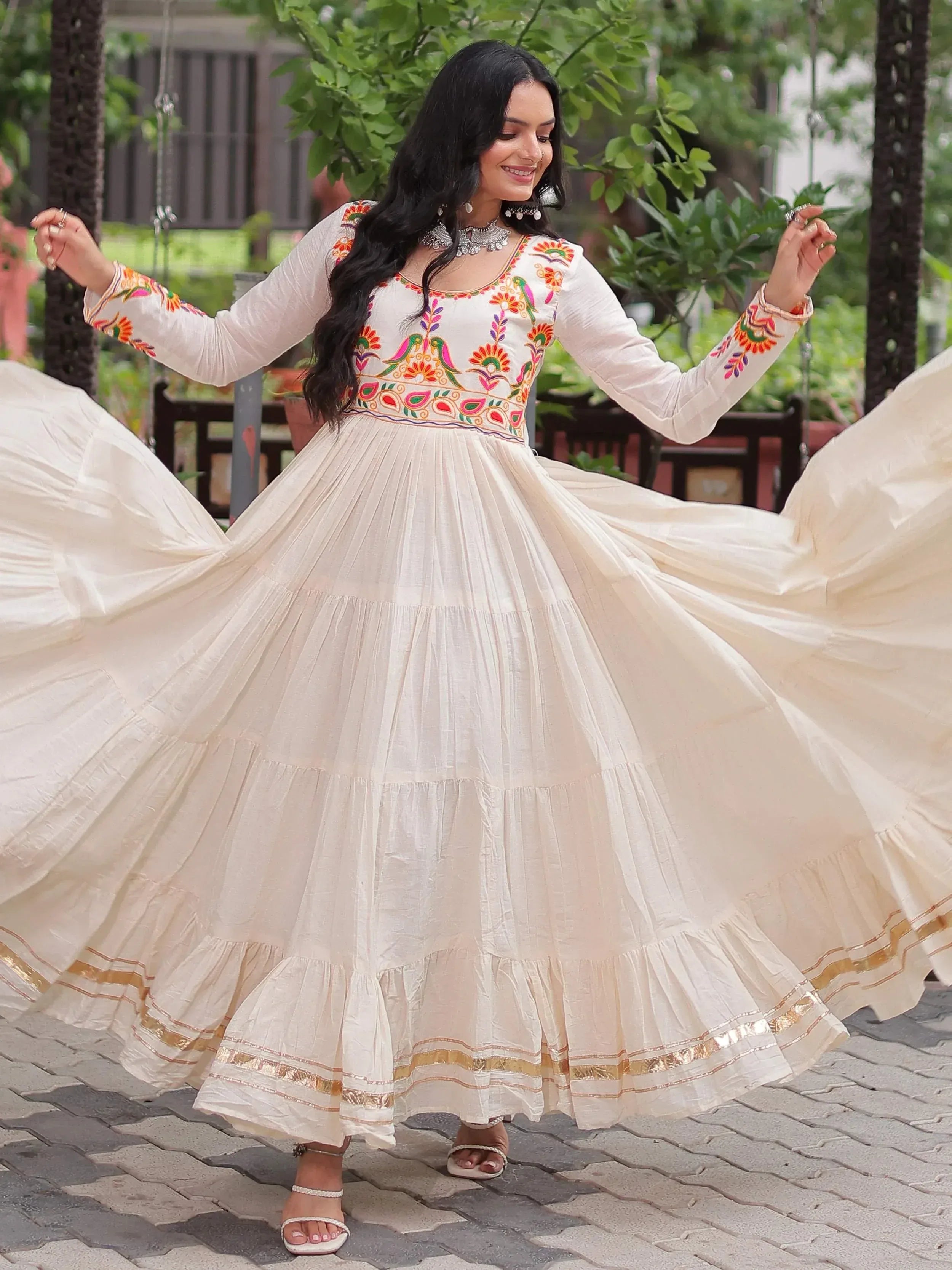Woman twirling in white embroidered ethnic gown with floral patterns and gold trim, perfect for Indian celebrations.