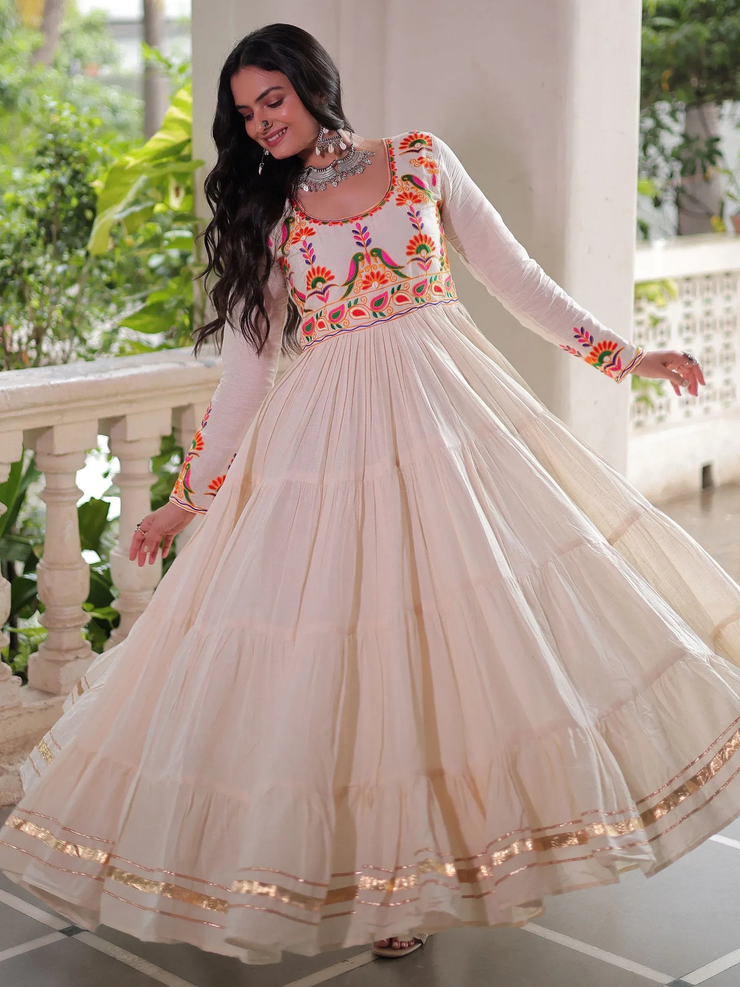 Woman in white ethnic gown with colorful embroidery and gold trim, twirling on balcony