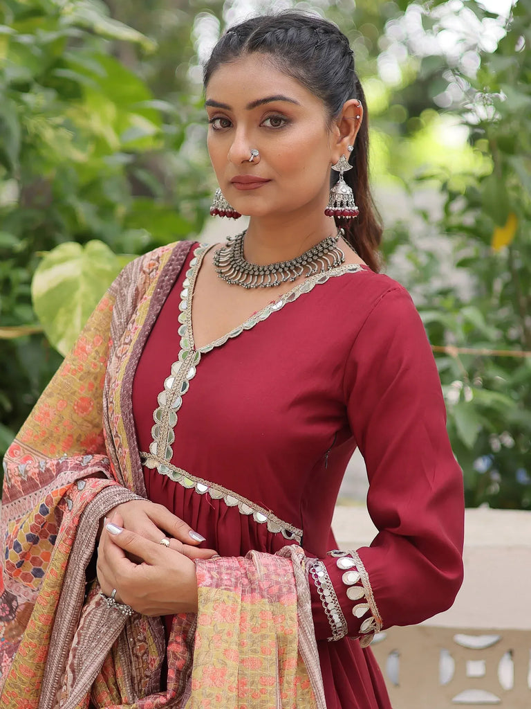 Maroon ethnic gown with mirror work and floral dupatta, styled with traditional jewelry for festive occasions