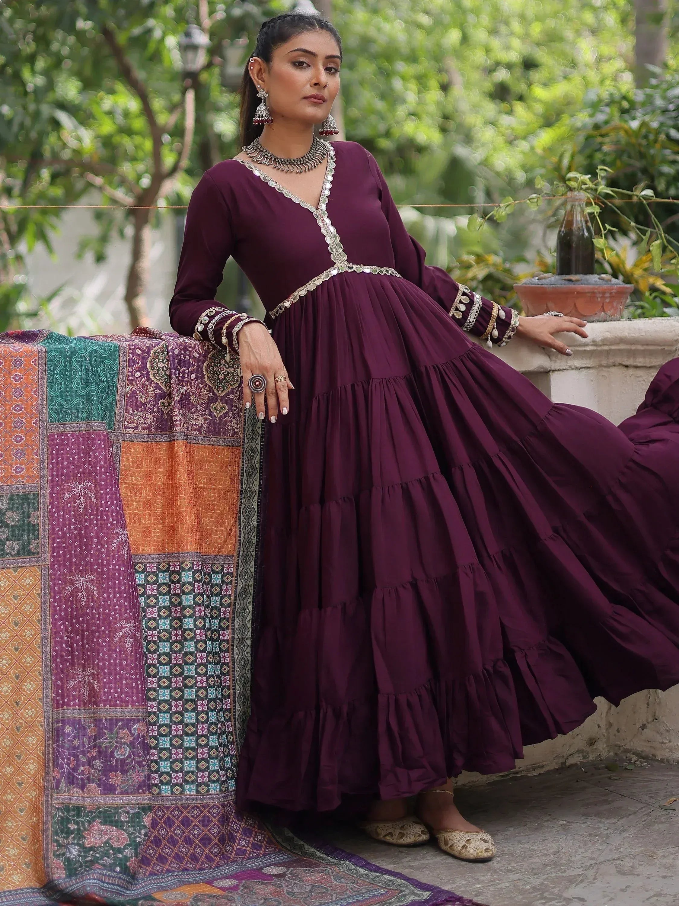 Elegant maroon ethnic gown with mirror work, tiered skirt, and traditional jewelry for Indian occasions