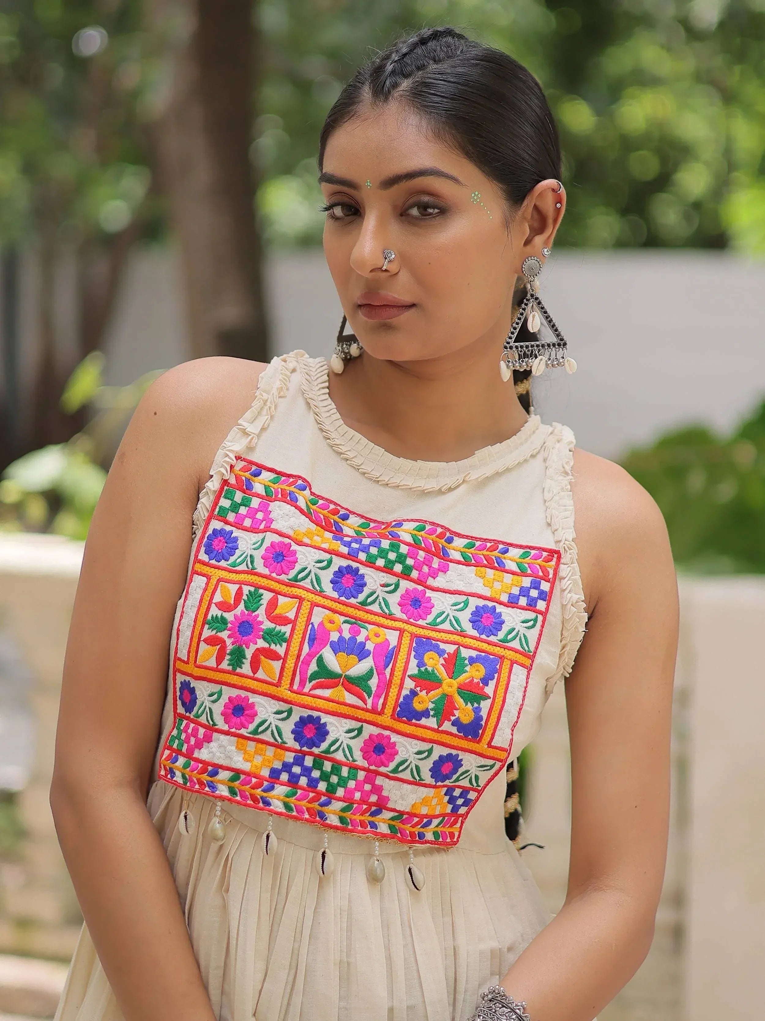 Woman in cream ethnic gown with colorful floral embroidery and traditional jewelry