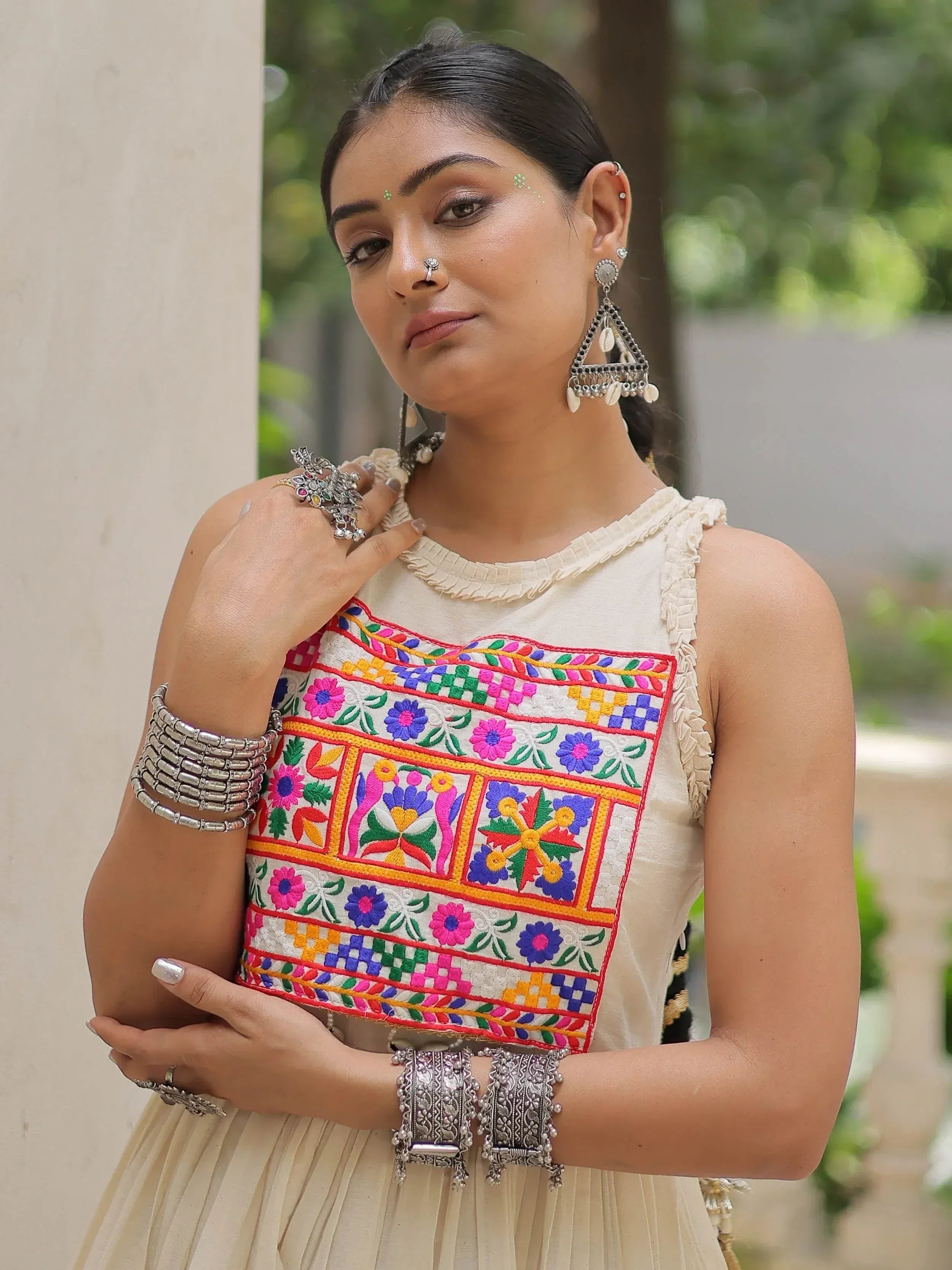 Woman in cream ethnic gown with colorful floral embroidery and traditional silver jewelry