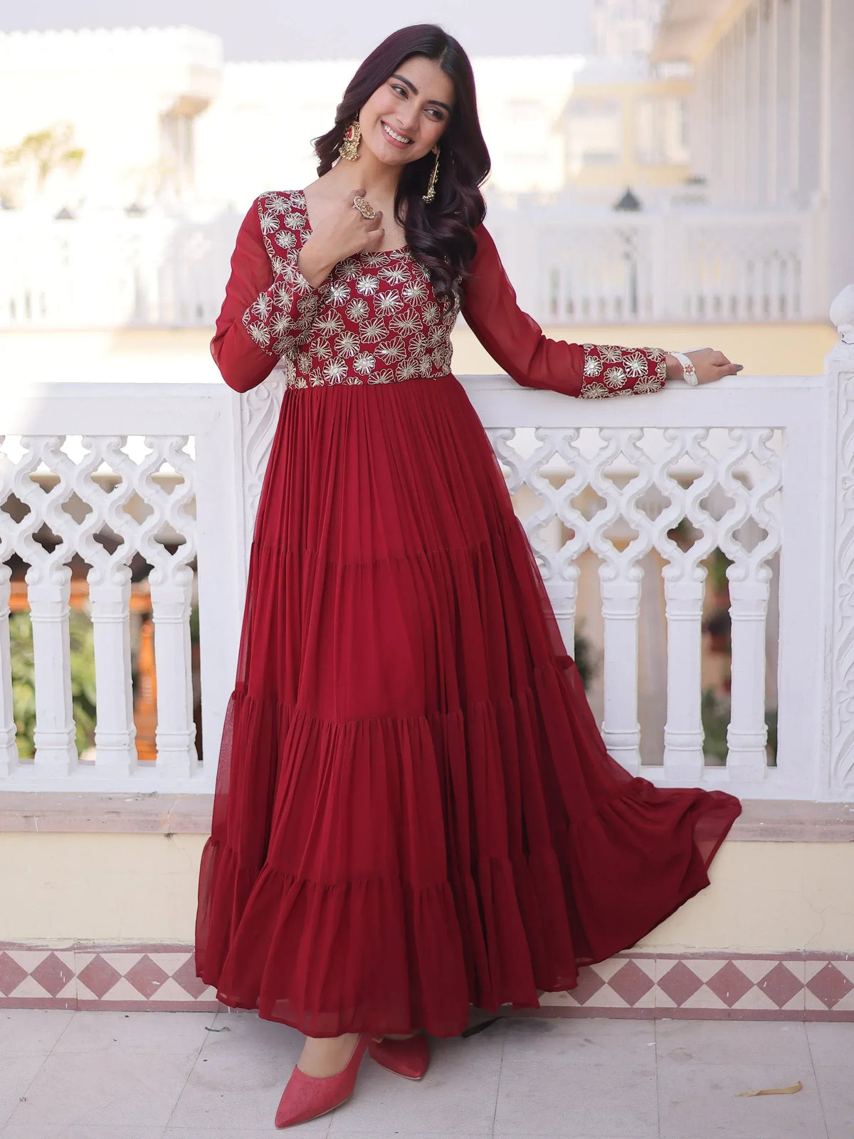 Woman in a red embroidered ethnic gown standing by a white carved balcony