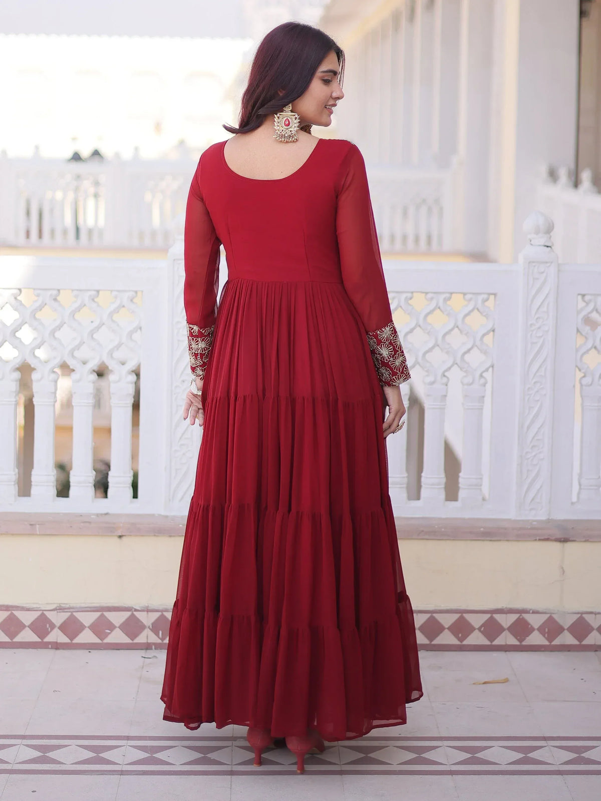Woman wearing a red tiered ethnic gown with embroidered sleeves and traditional earrings.