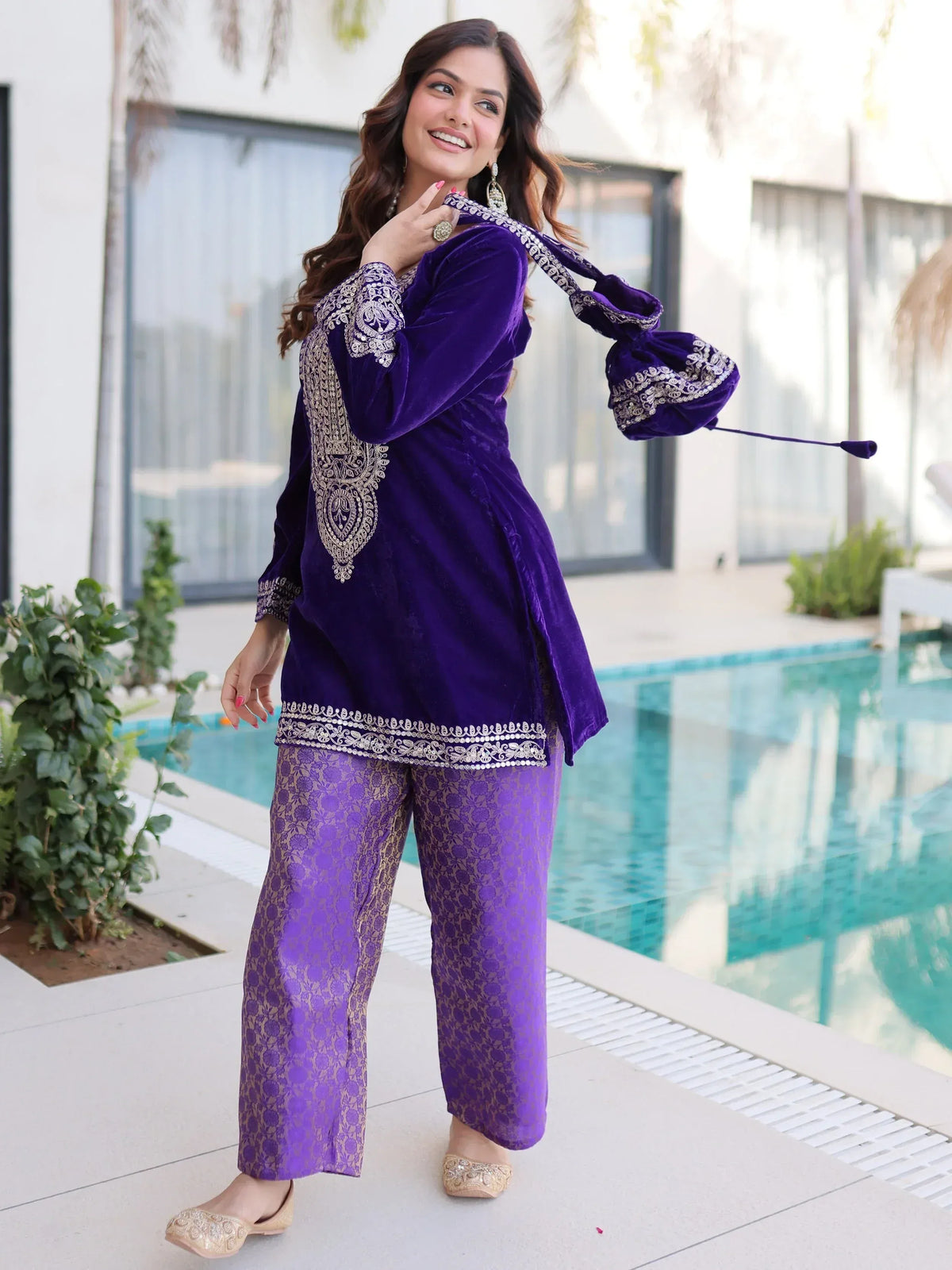 Purple velvet ethnic suit with gold embroidery, palazzo pants, and matching potli bag by poolside