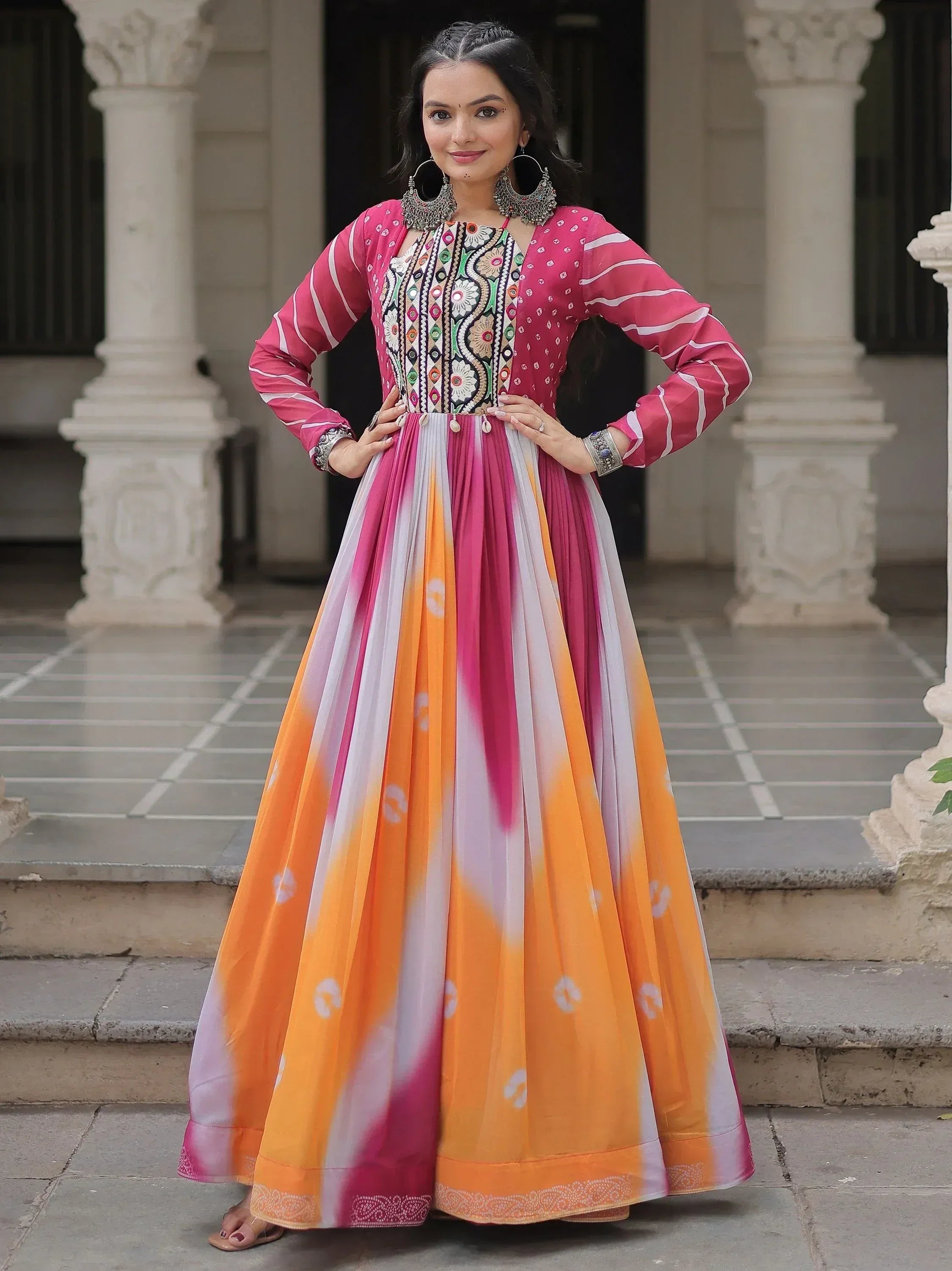 Woman in vibrant pink and orange ethnic gown with embroidered top and pleated skirt, perfect for Indian festivals.