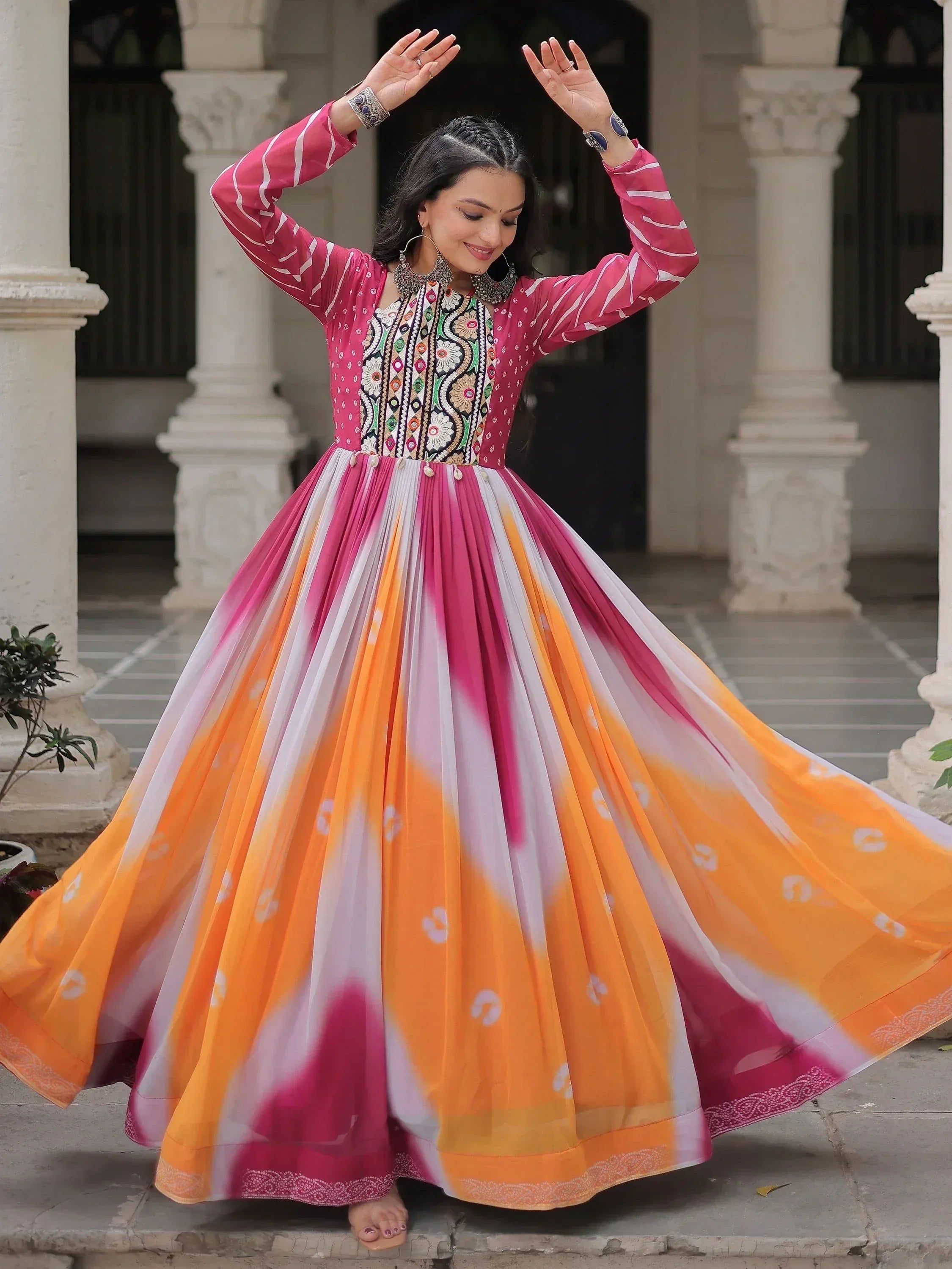 Woman in vibrant pink and orange ethnic gown with floral embroidery, dancing gracefully in courtyard