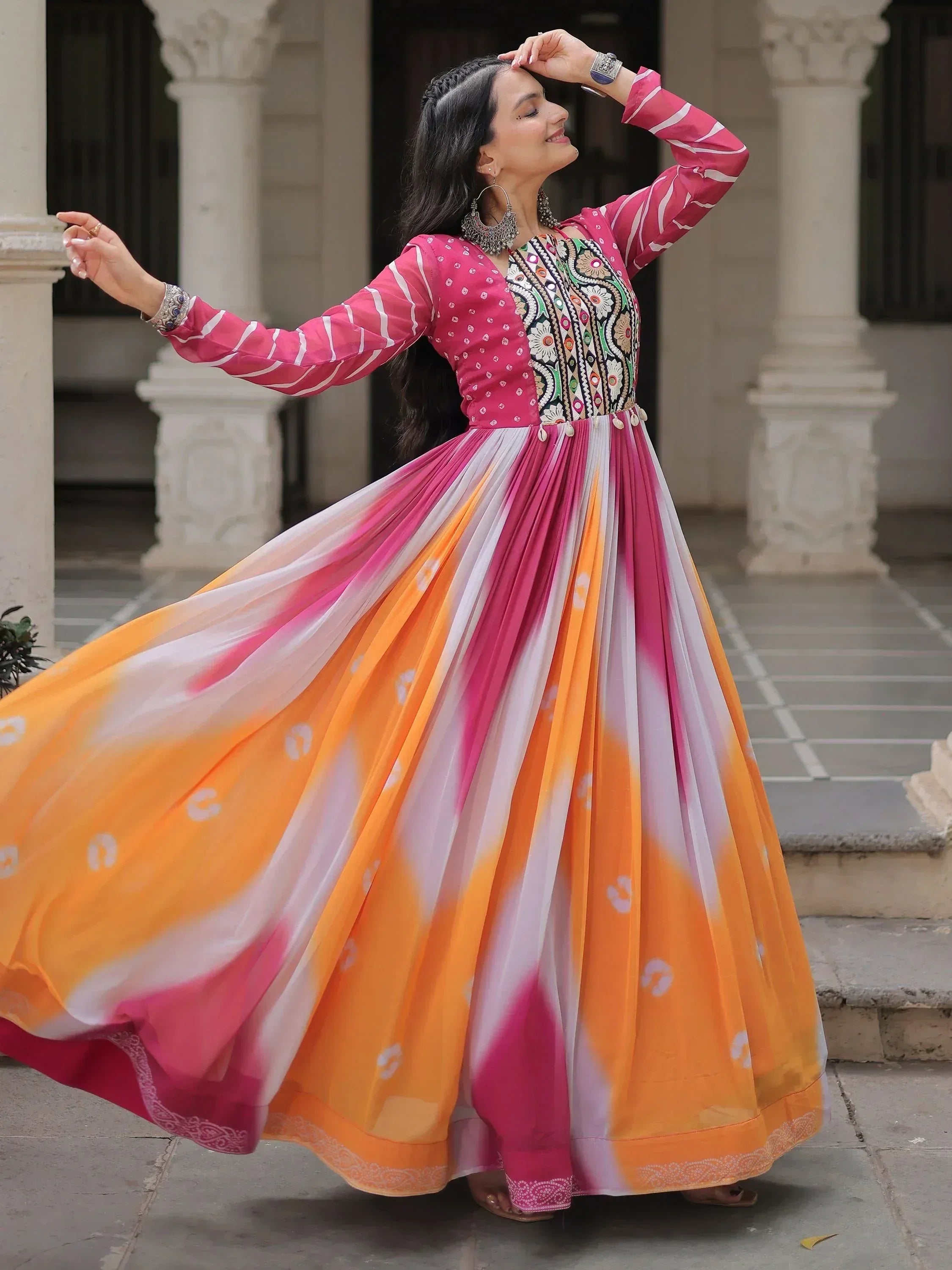 Woman in vibrant pink and orange ethnic gown with embroidered top, twirling outdoors