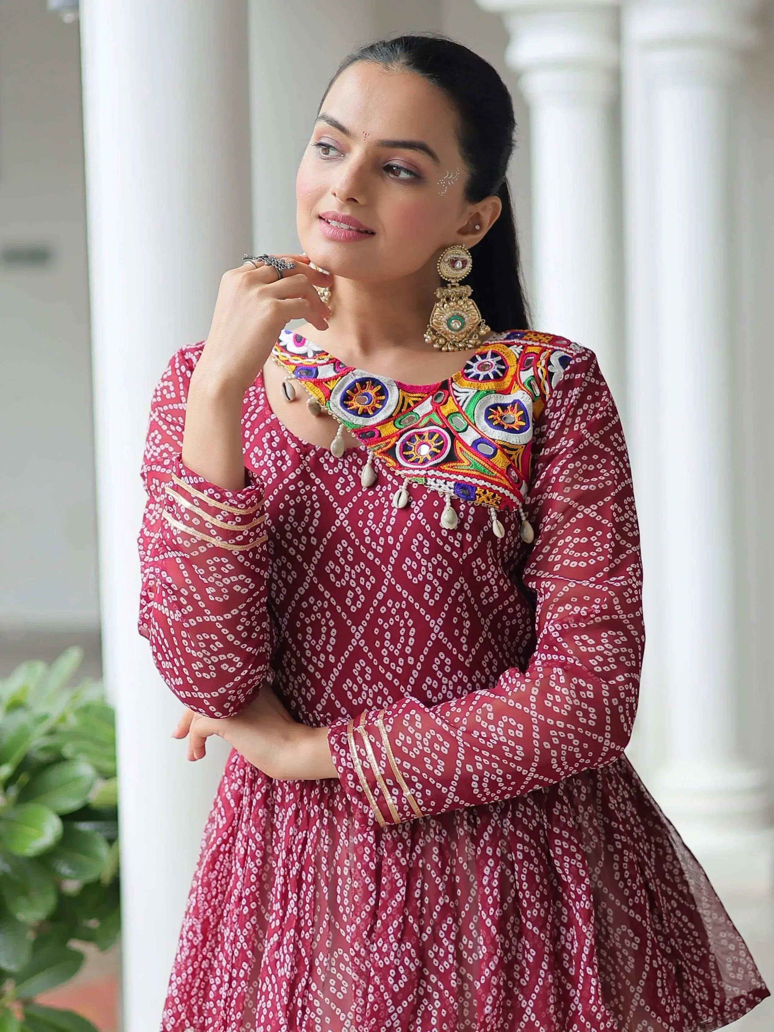 Woman in maroon ethnic gown with mirror embroidery and traditional jewelry, perfect for Indian festive occasions.