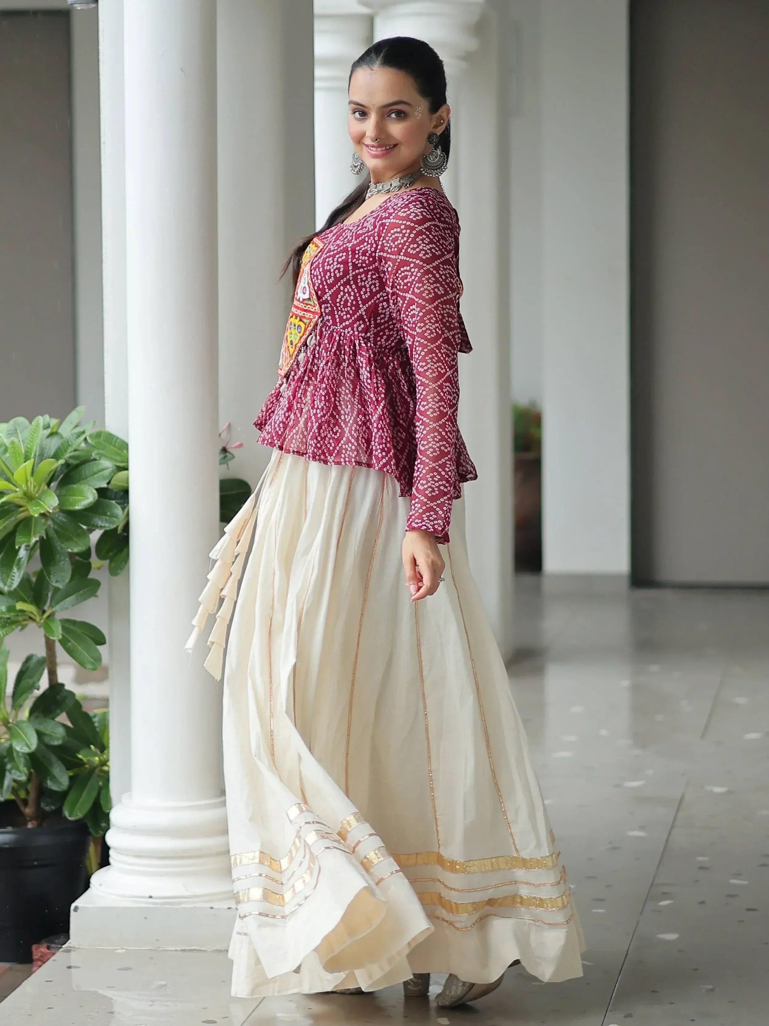 Woman in maroon printed blouse with off-white lehenga, gold trim, and traditional jewelry