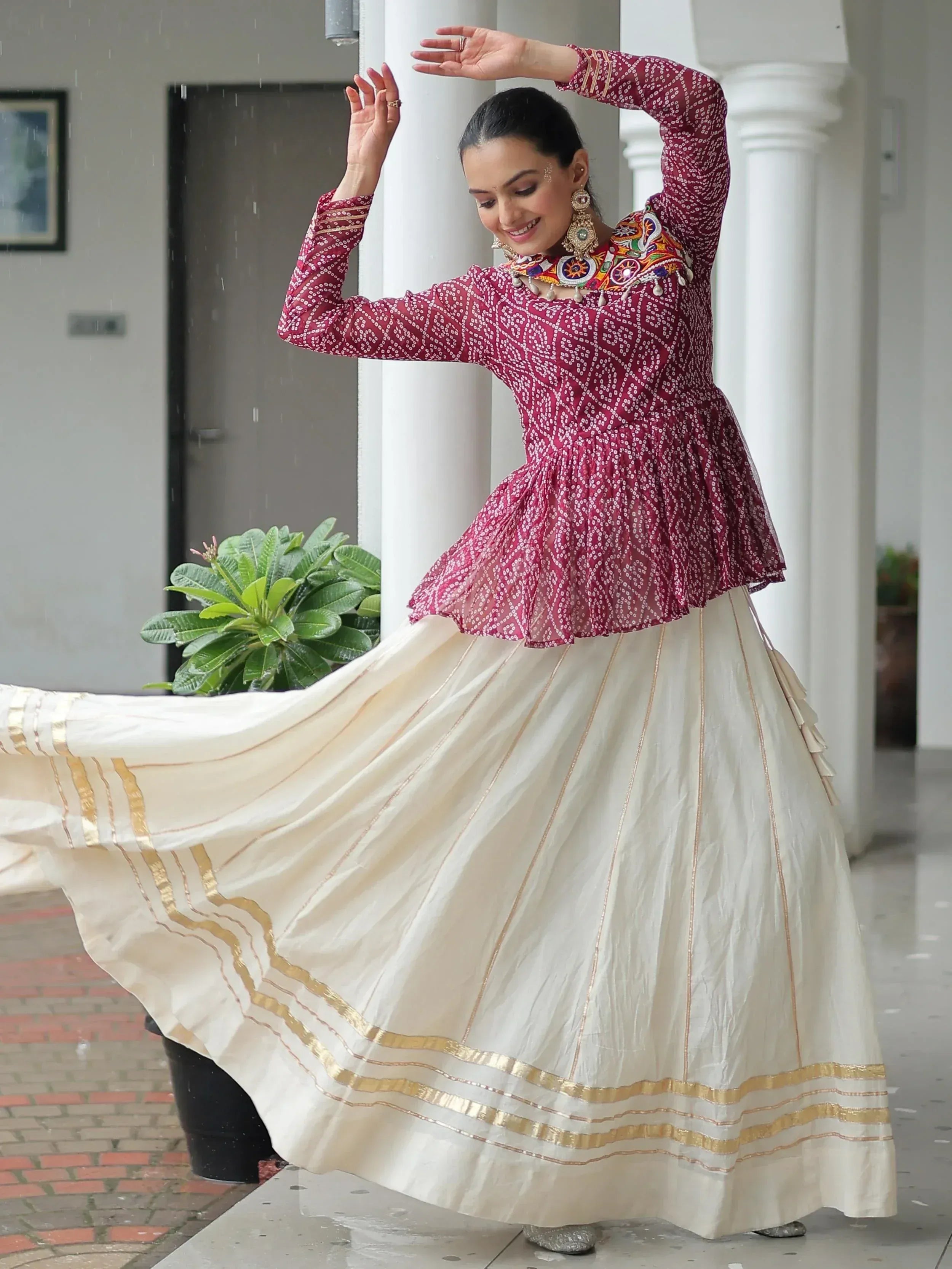 Woman dancing in maroon printed top with embroidered neckline and cream pleated skirt with gold trim, Indian ethnic wear