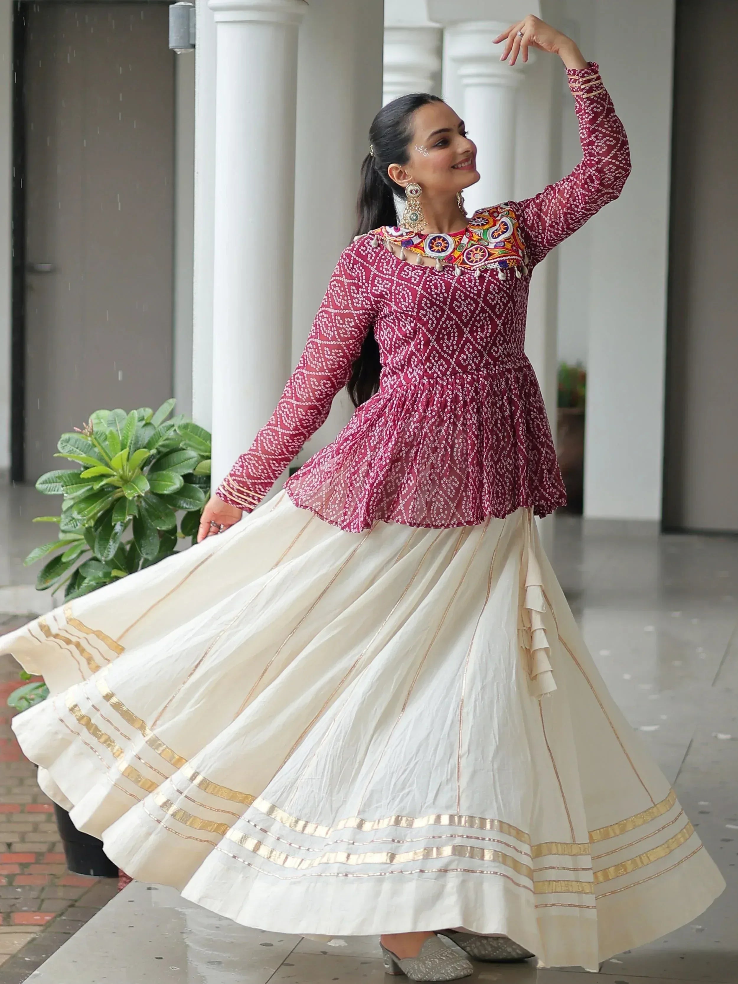 Woman twirling in maroon embroidered top and cream pleated skirt, Indian ethnic wear