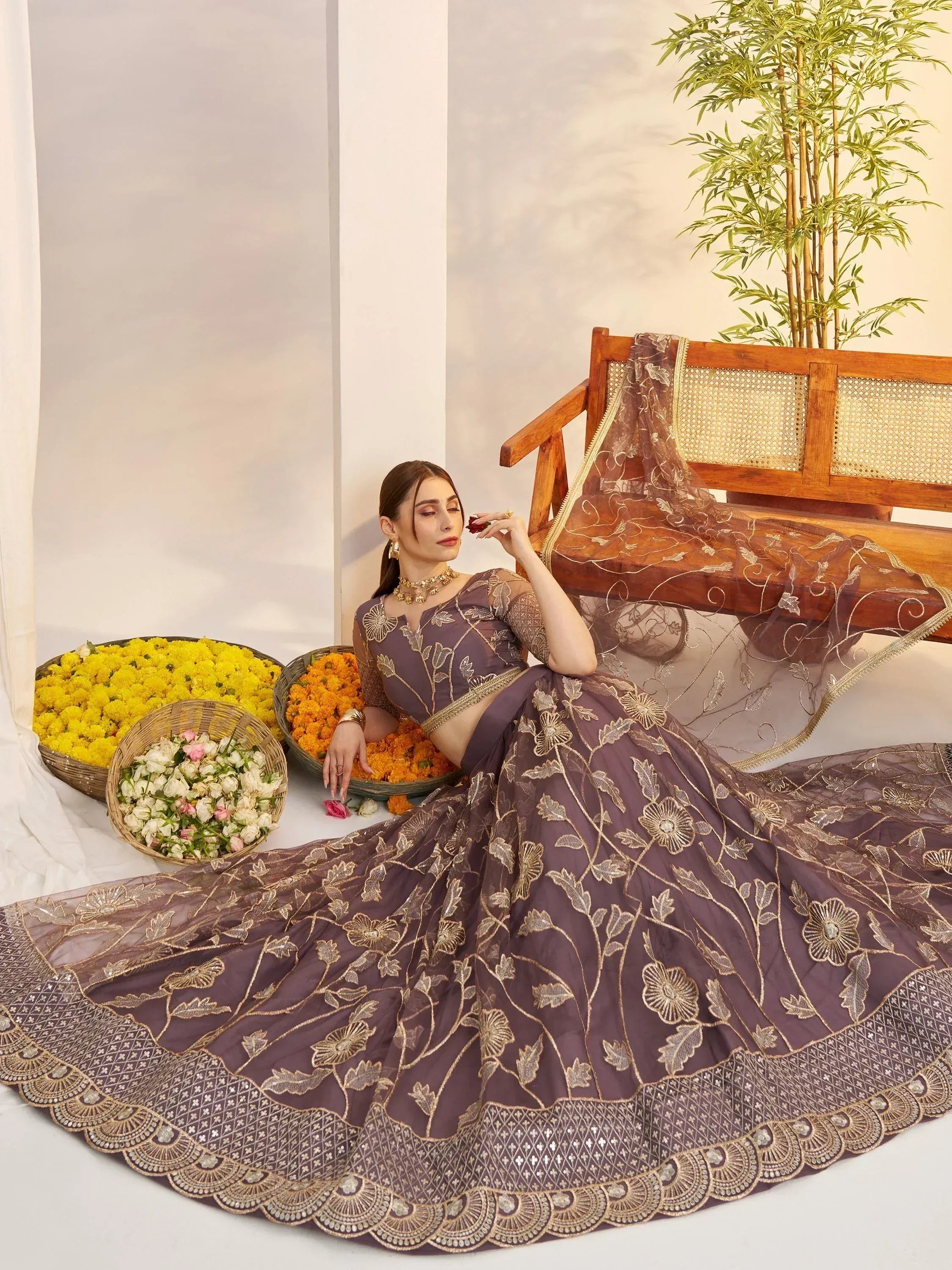 Elegant purple lehenga choli with gold floral embroidery, styled with flowers and a wooden bench.