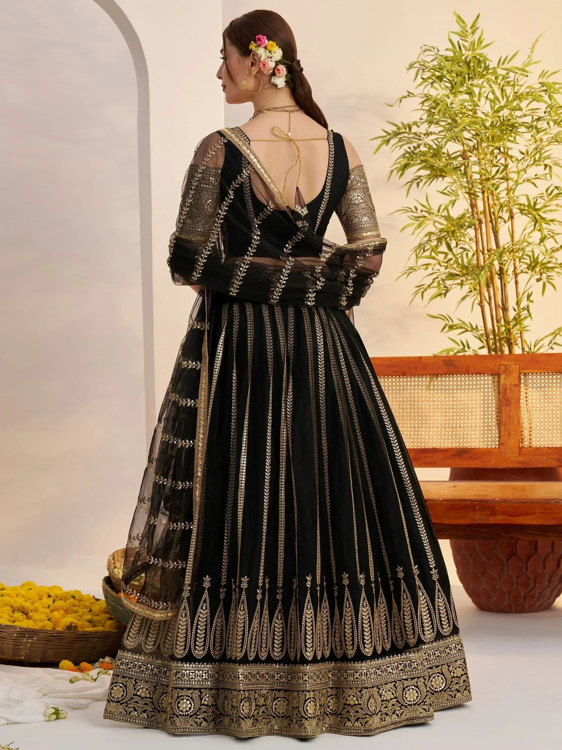 Black and gold embroidered lehenga choli with sheer sleeves, floral hair accessory, and back detailing