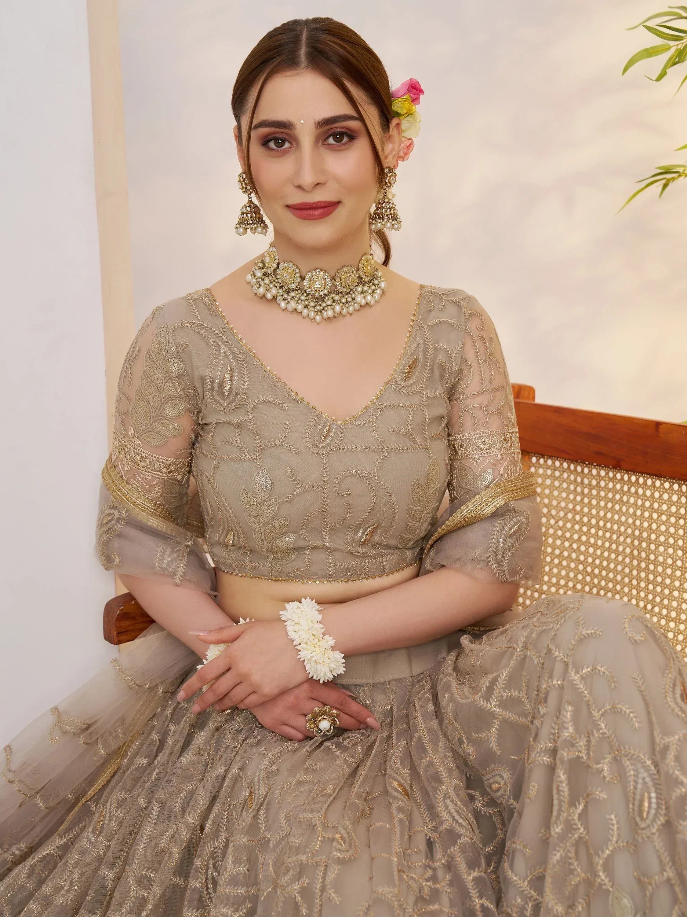 Elegant beige embroidered lehenga choli with gold detailing, floral hair accessory, and pearl jewelry for Indian ethnic wear.