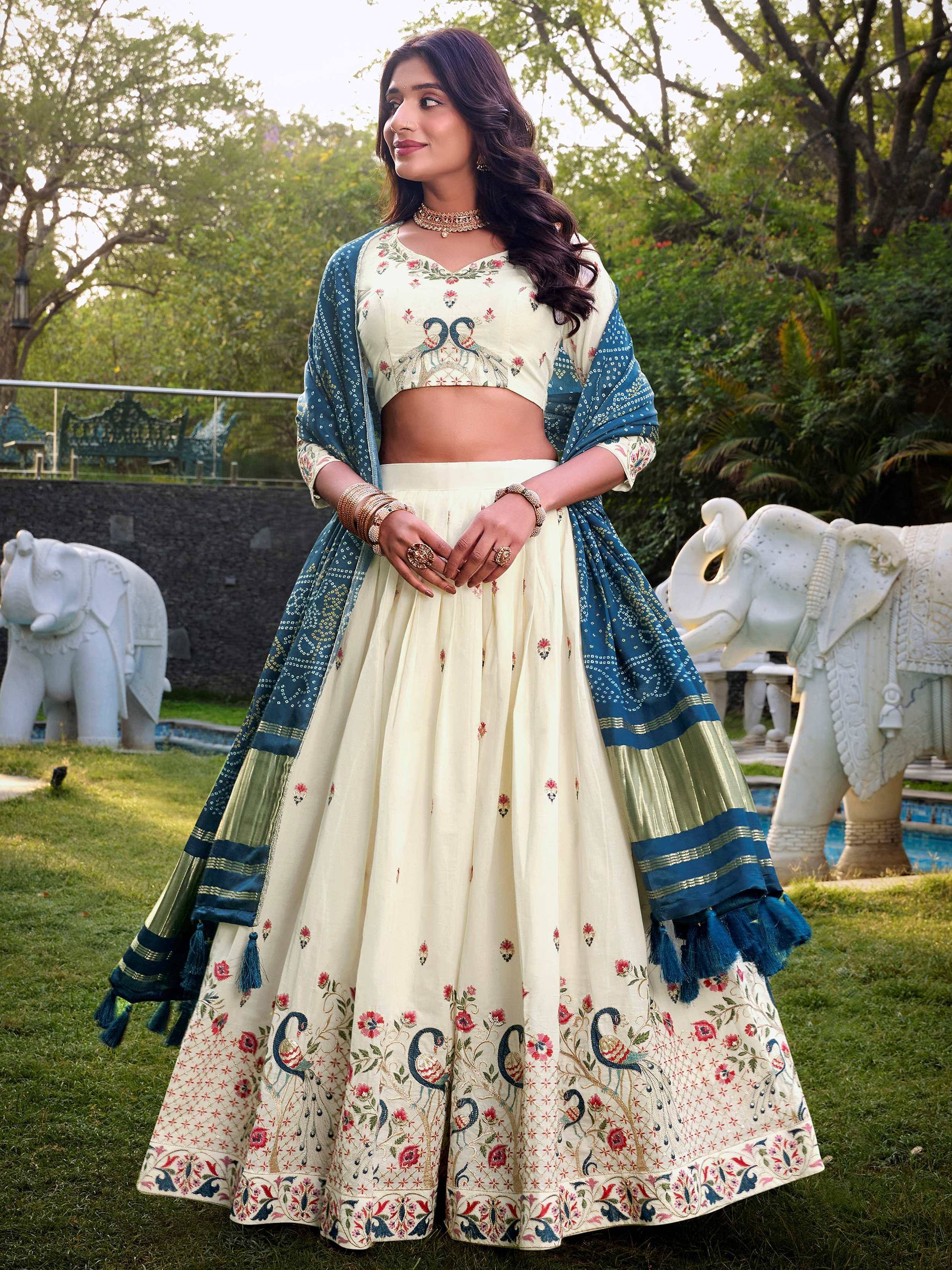 Cream embroidered lehenga choli with peacock motifs, blue dupatta, garden setting