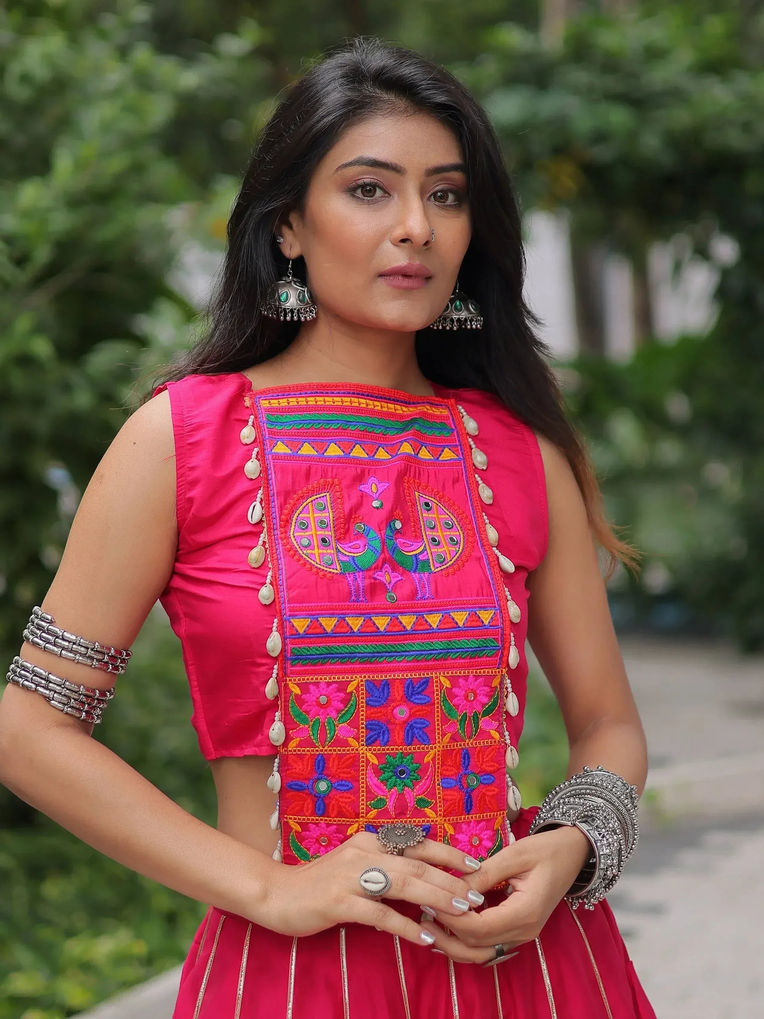 Woman in vibrant pink ethnic wear with peacock embroidery, traditional jewelry, and mirror work for festive occasions.