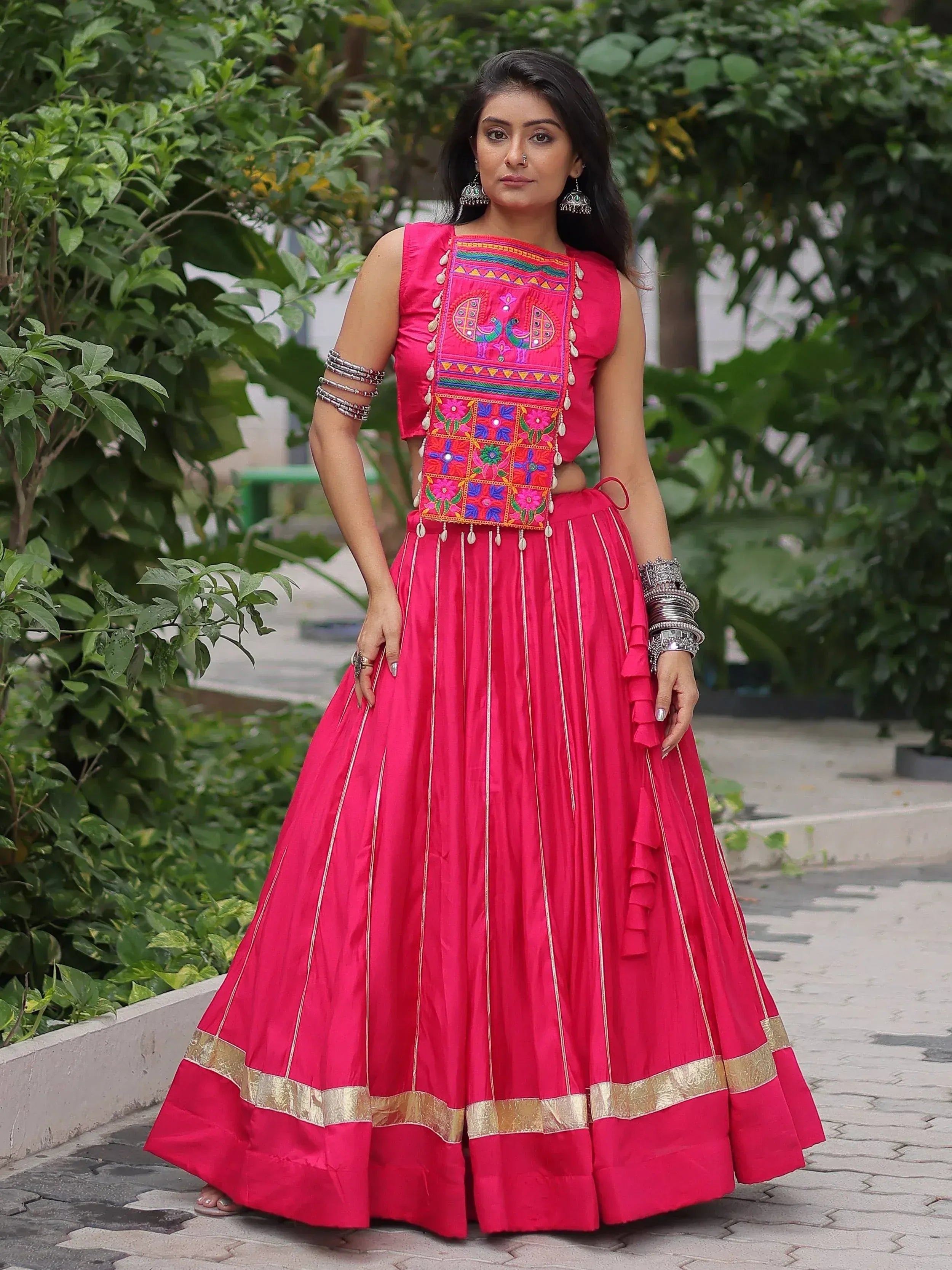 Vibrant pink embroidered lehenga choli with peacock motifs, gold trim, and traditional jewelry for Indian ethnic wear