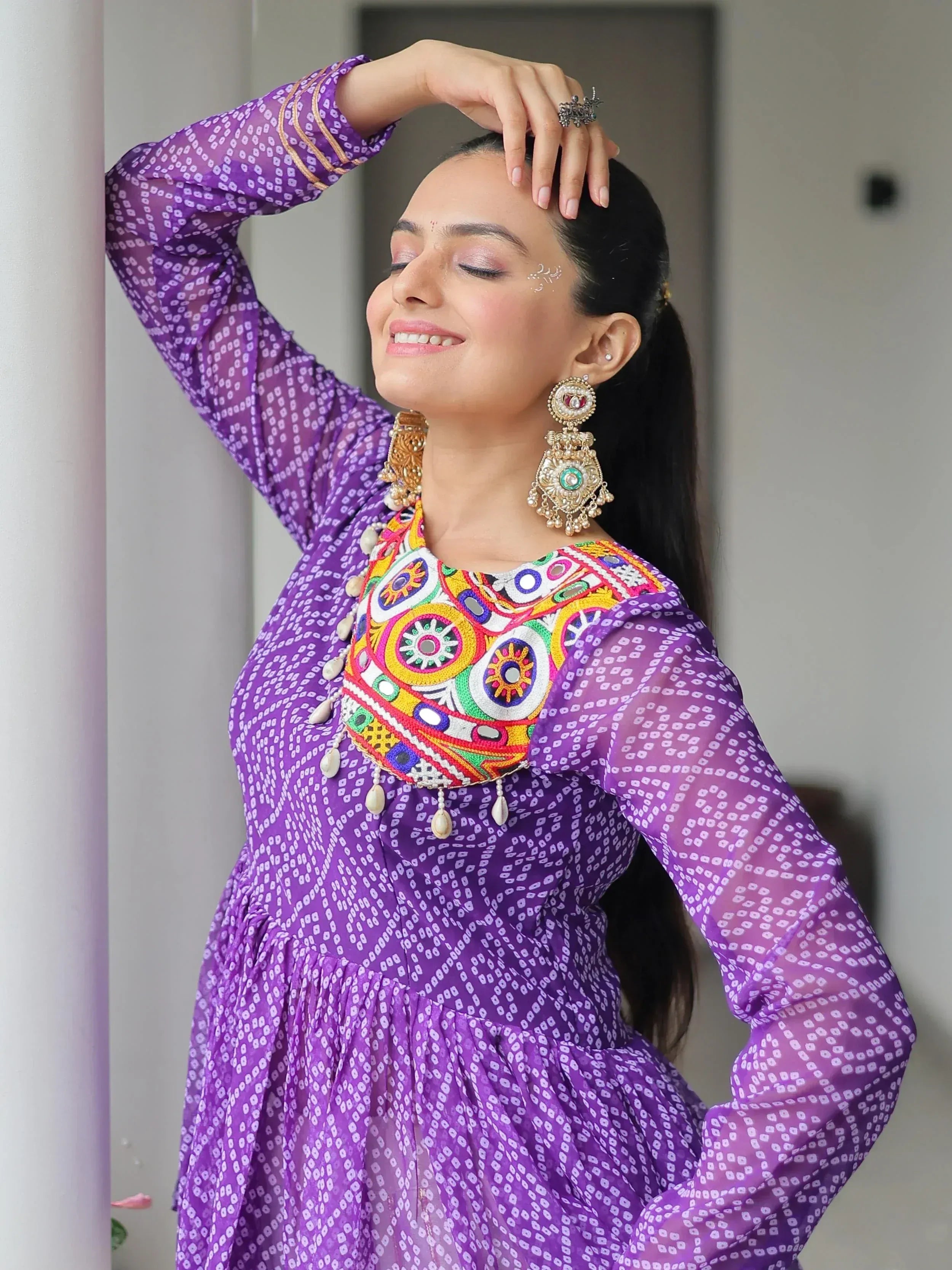 Purple ethnic kurti with colorful mirror work and sheer sleeves, paired with traditional jhumka earrings