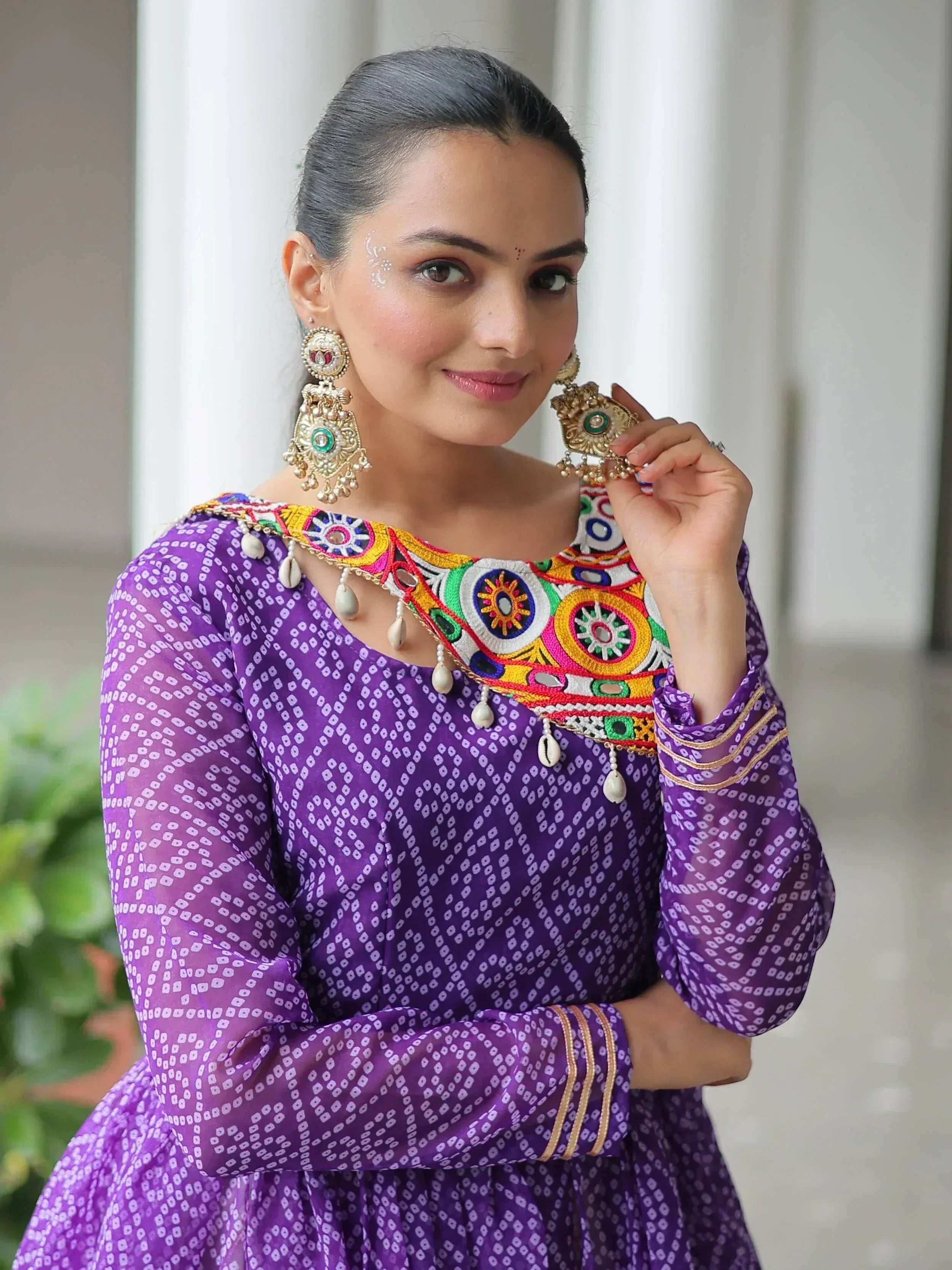 Purple ethnic gown with colorful embroidery and mirror work, paired with traditional jhumka earrings