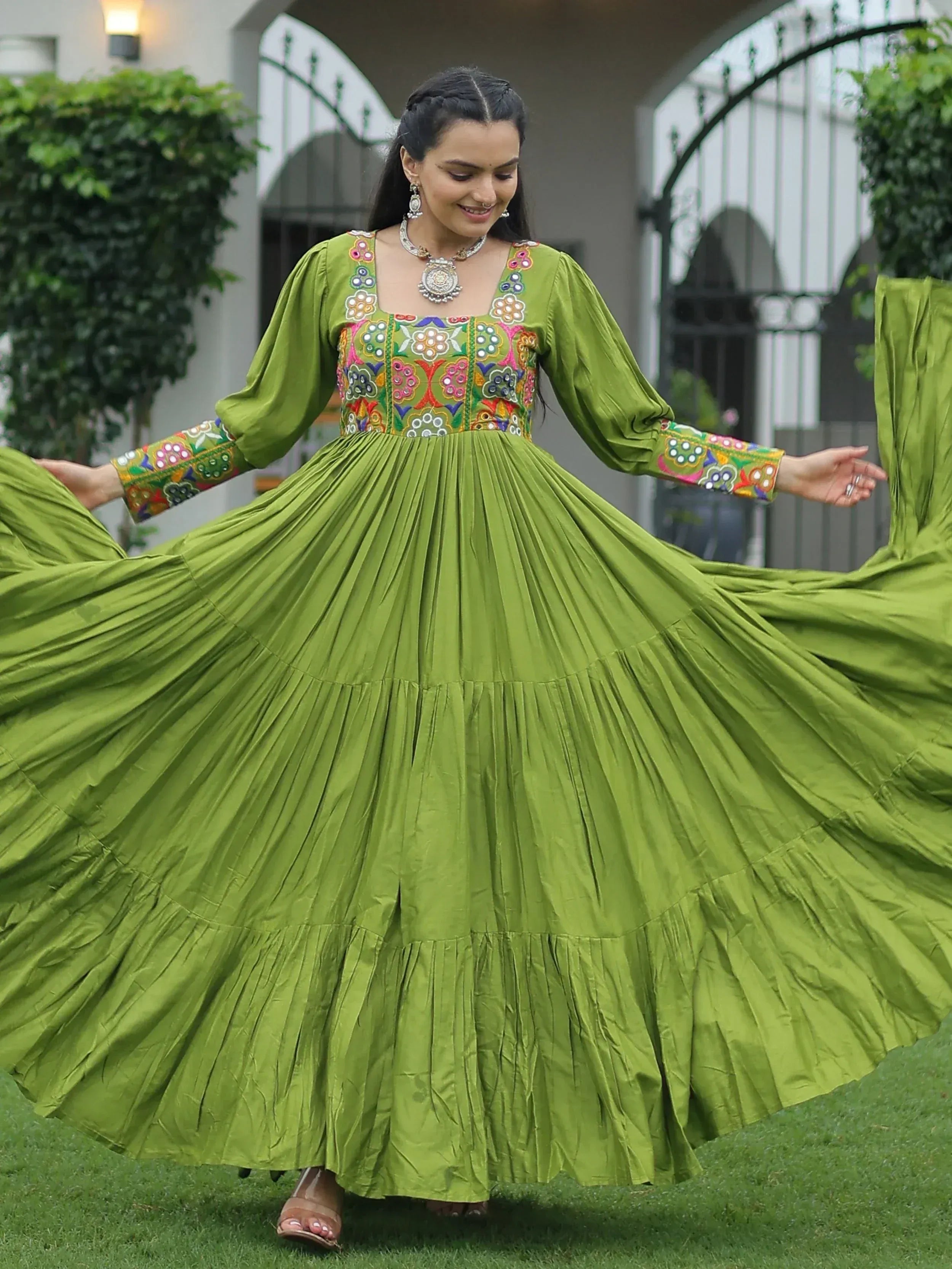 Woman twirling in vibrant green ethnic gown with colorful floral embroidery, perfect for festive occasions.