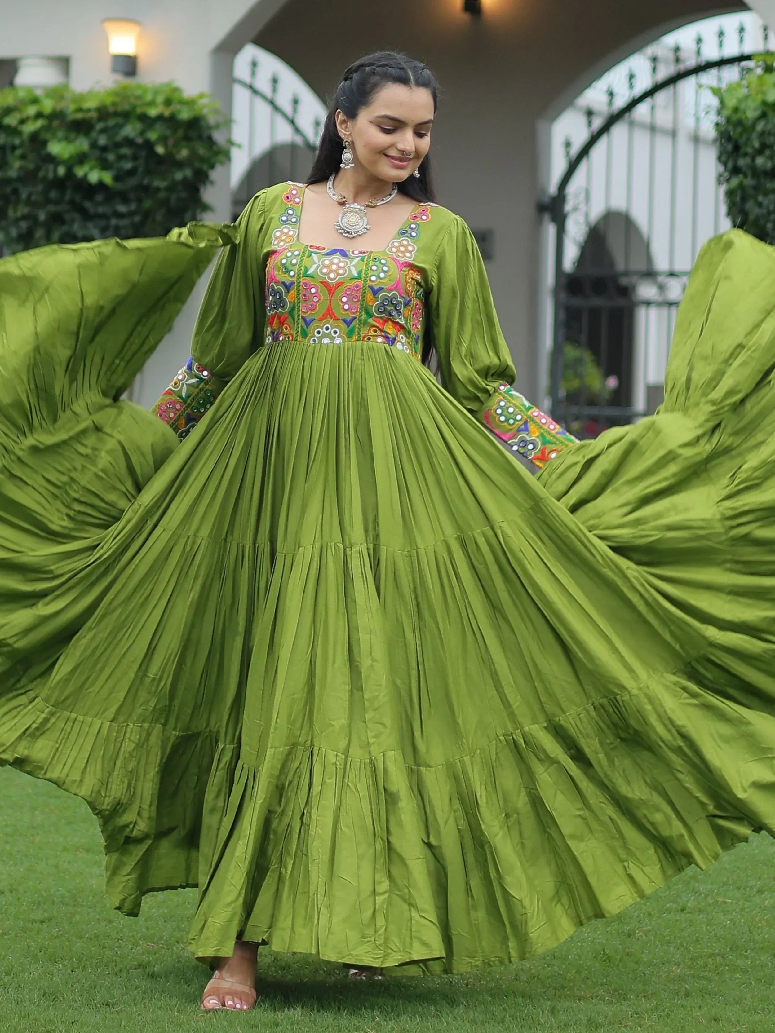 Woman twirling in vibrant green ethnic gown with colorful embroidery, perfect for festive occasions.