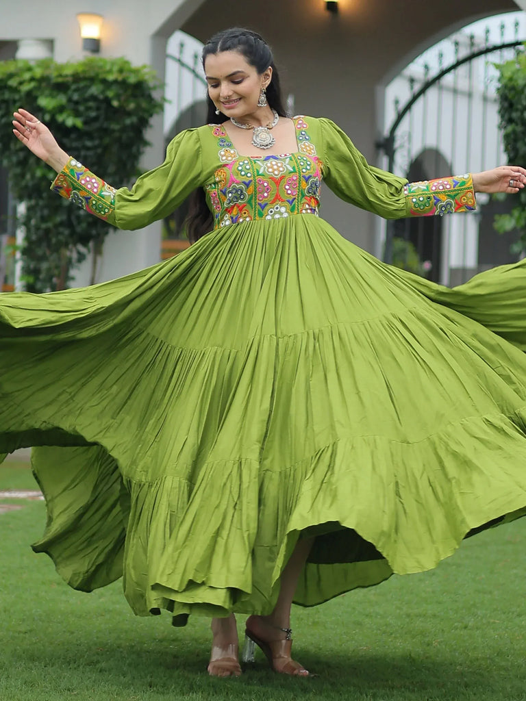 Woman twirling in vibrant green ethnic gown with colorful floral embroidery, perfect for festive occasions.