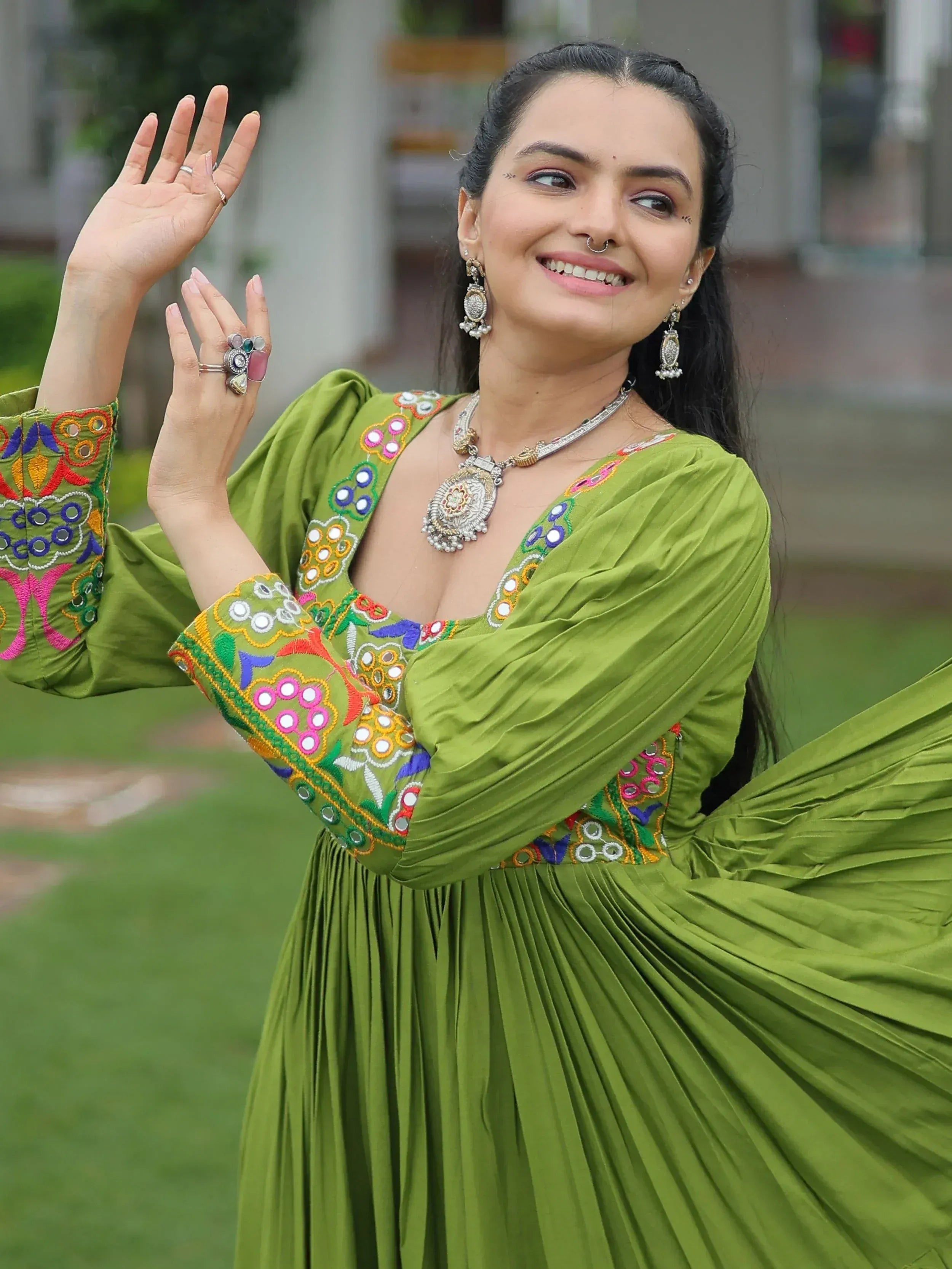 Woman in green embroidered ethnic gown with mirror work, traditional jewelry, dancing outdoors