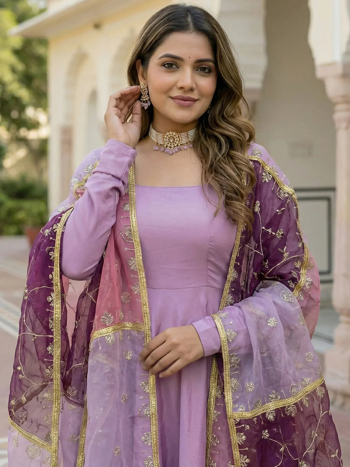 Elegant lavender ethnic gown with gold embroidery and sheer dupatta, perfect for Indian celebrations.